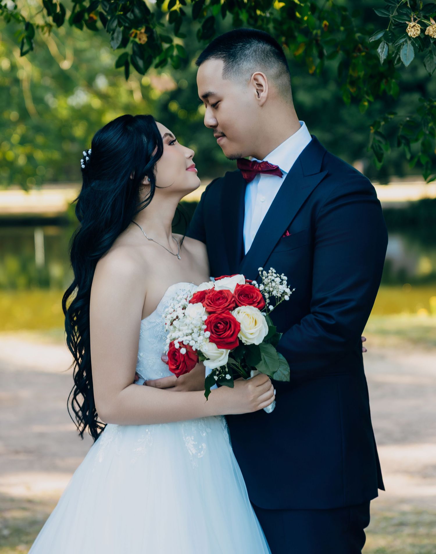 Newlyweds sharing romantic moment outdoors, bride holding red and white rose bouquet.