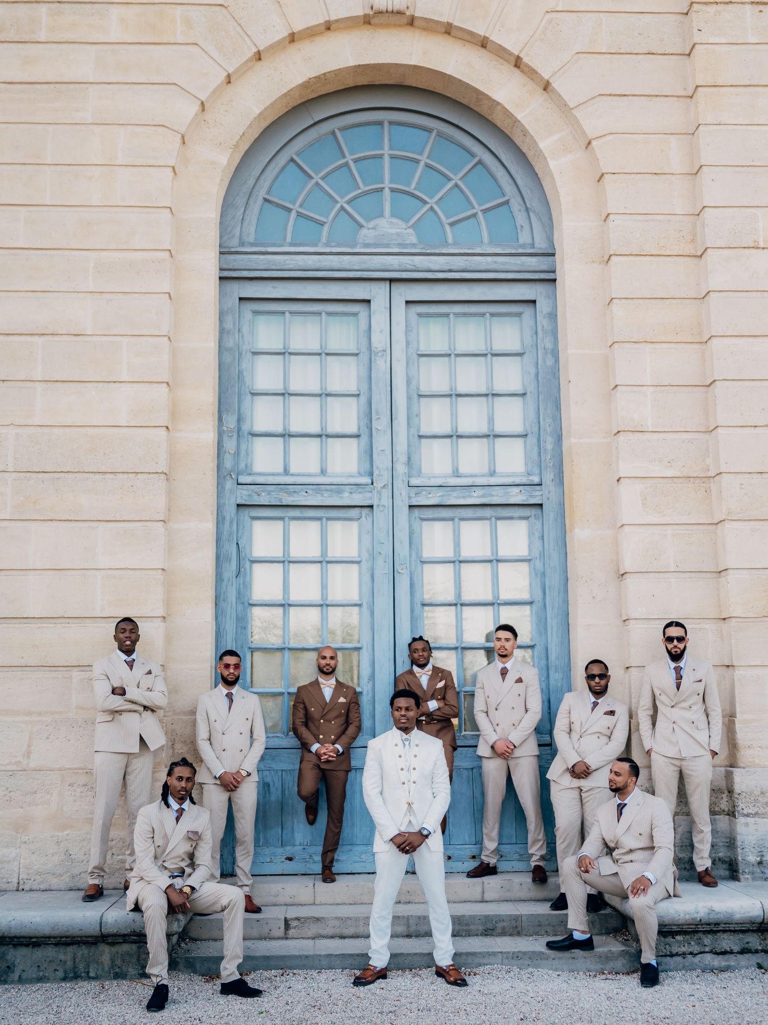 Wedding party poses formally before elegant arched blue door at French chateau.