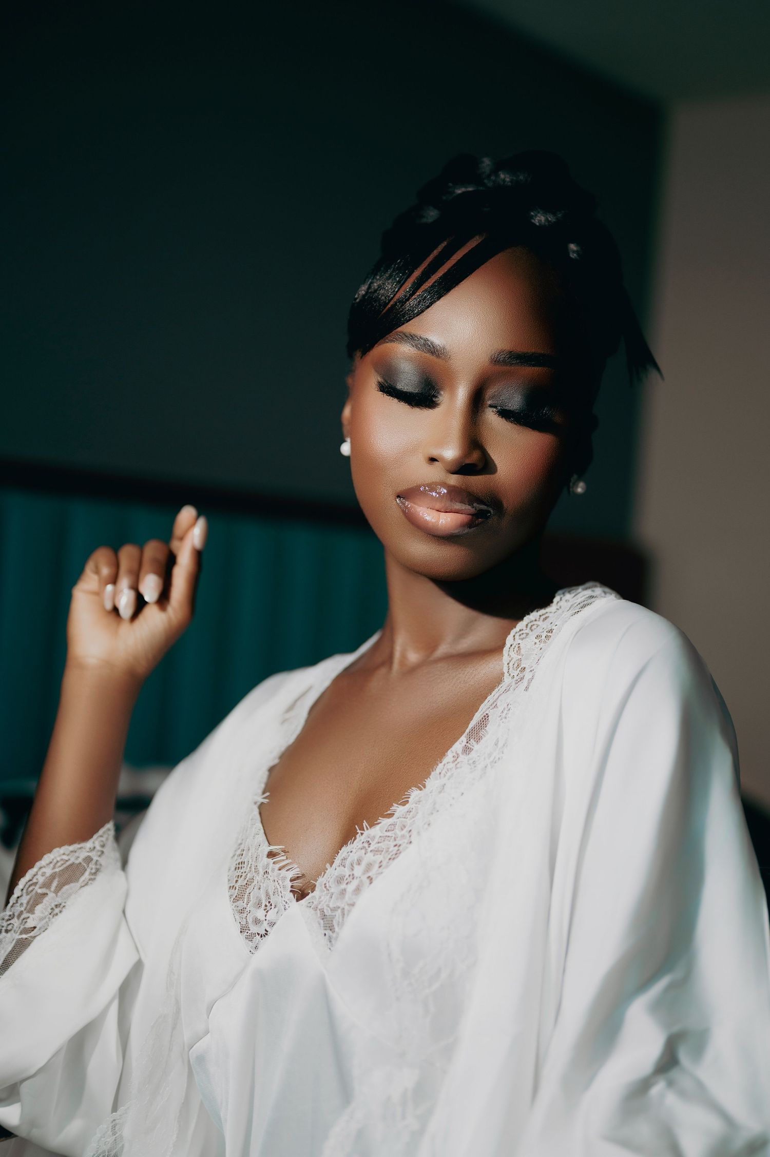 Bride in white lace robe with elegant updo and smoky eye makeup.