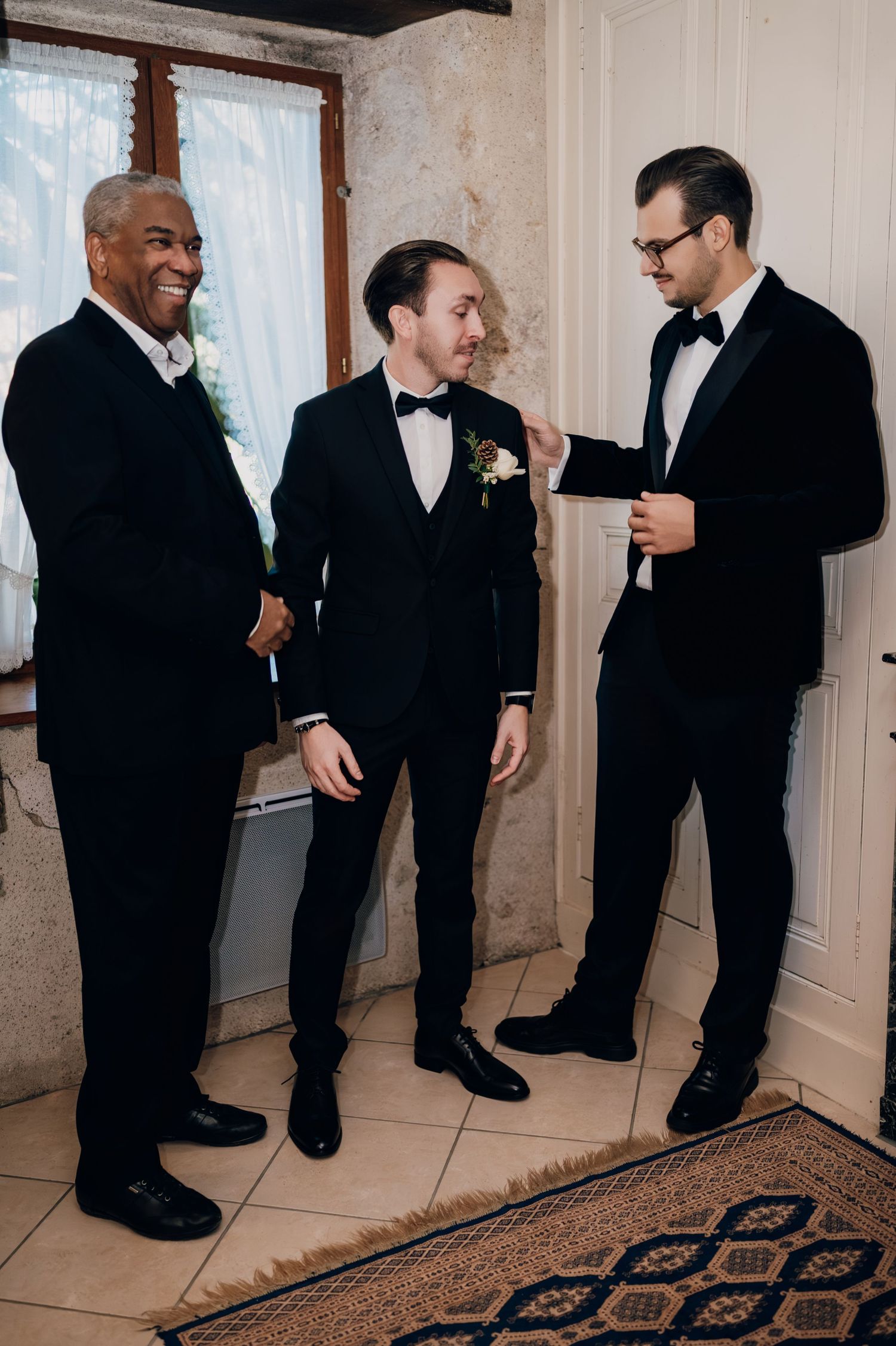 Three men in black tuxedos laughing and sharing a joyful moment before a wedding ceremony.
