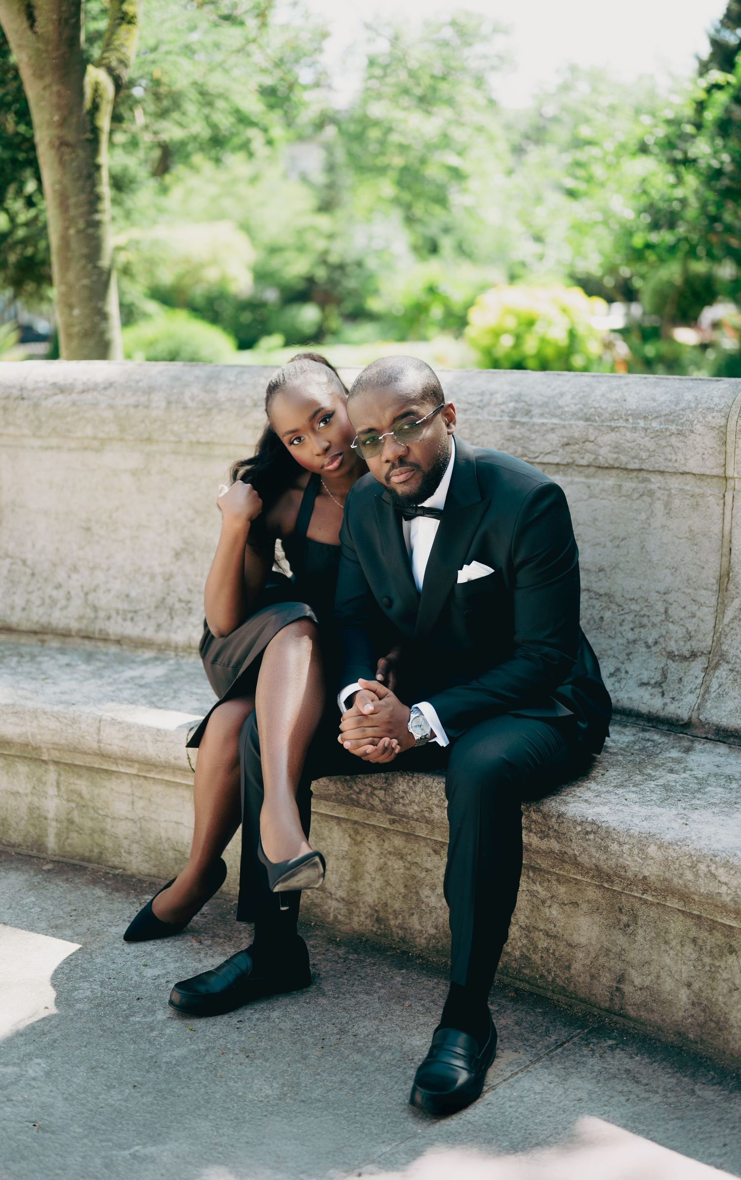 Sophisticated Black couple in formal black attire sit together on stone steps outdoors.
