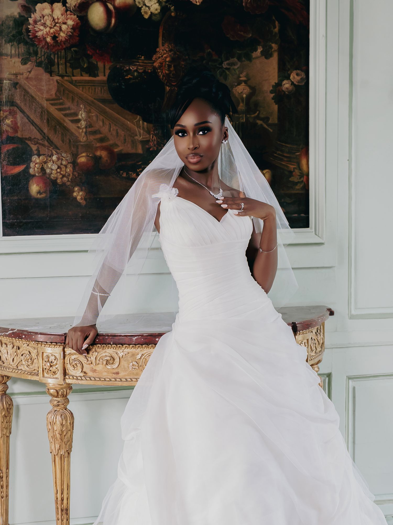 Elegant Black bride in a white strapless wedding gown with veil poses gracefully indoors.