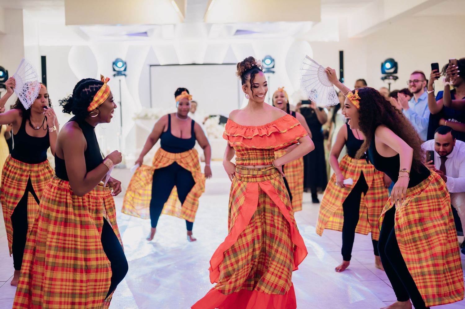 Bride in vibrant madras dress performing traditional Caribbean dance with dancers.