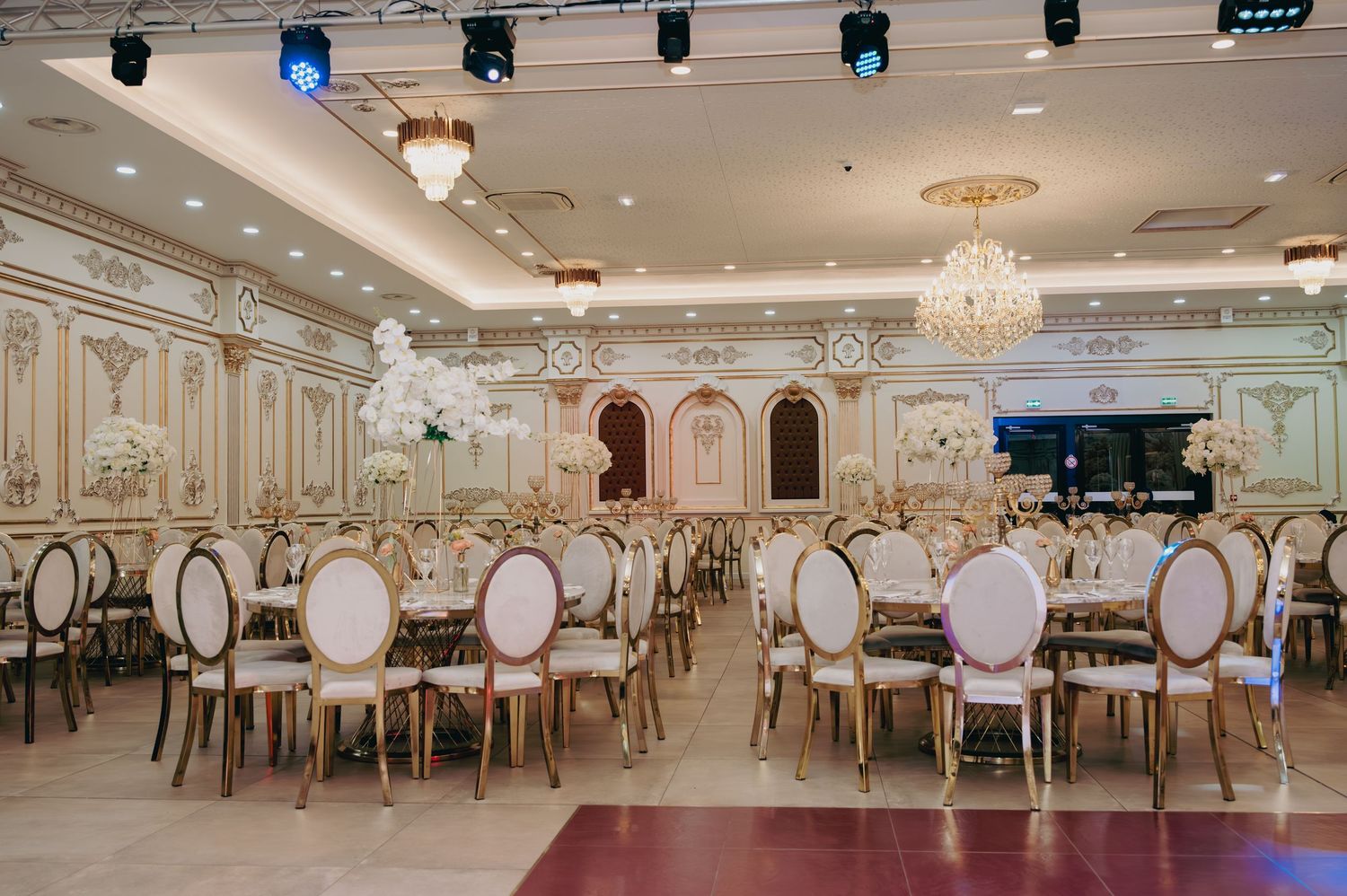 Grand wedding reception hall with gold and white chairs, chandeliers, and ornate decorative details.