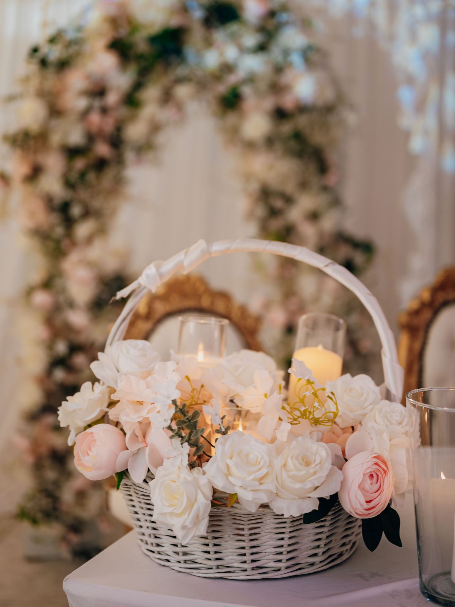 White wicker basket filled with white and blush roses and candles at elegant wedding reception.
