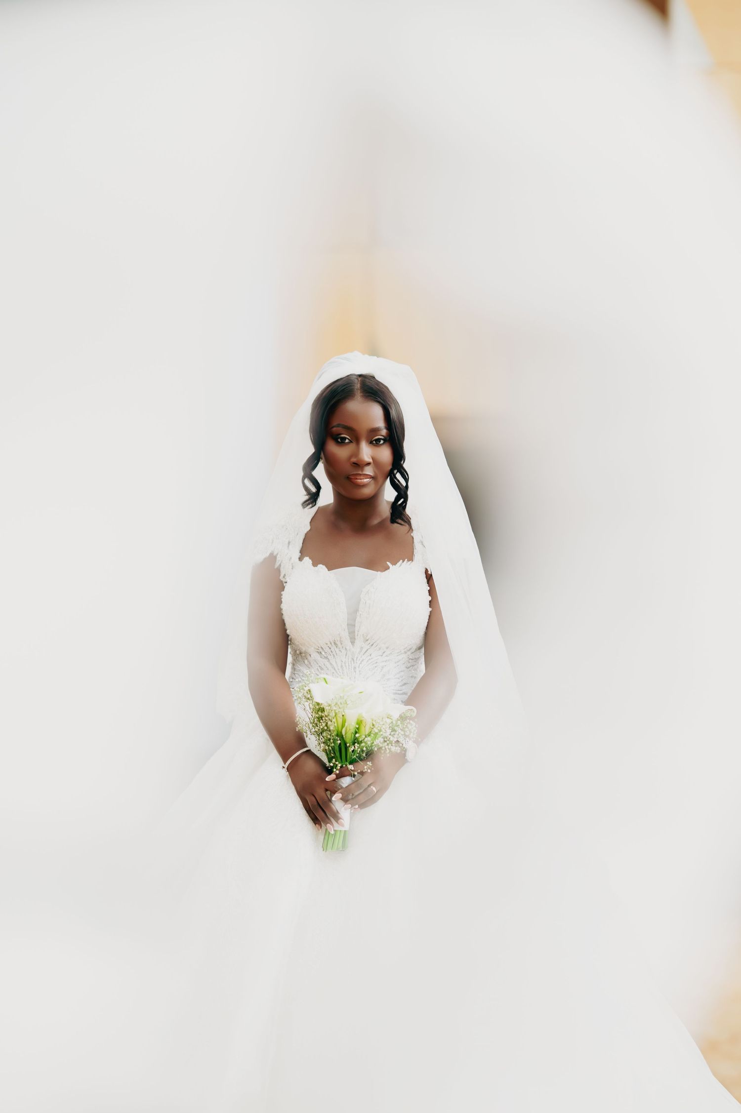 Beautiful bride in lace ball gown with veil holding white bouquet captured from above.