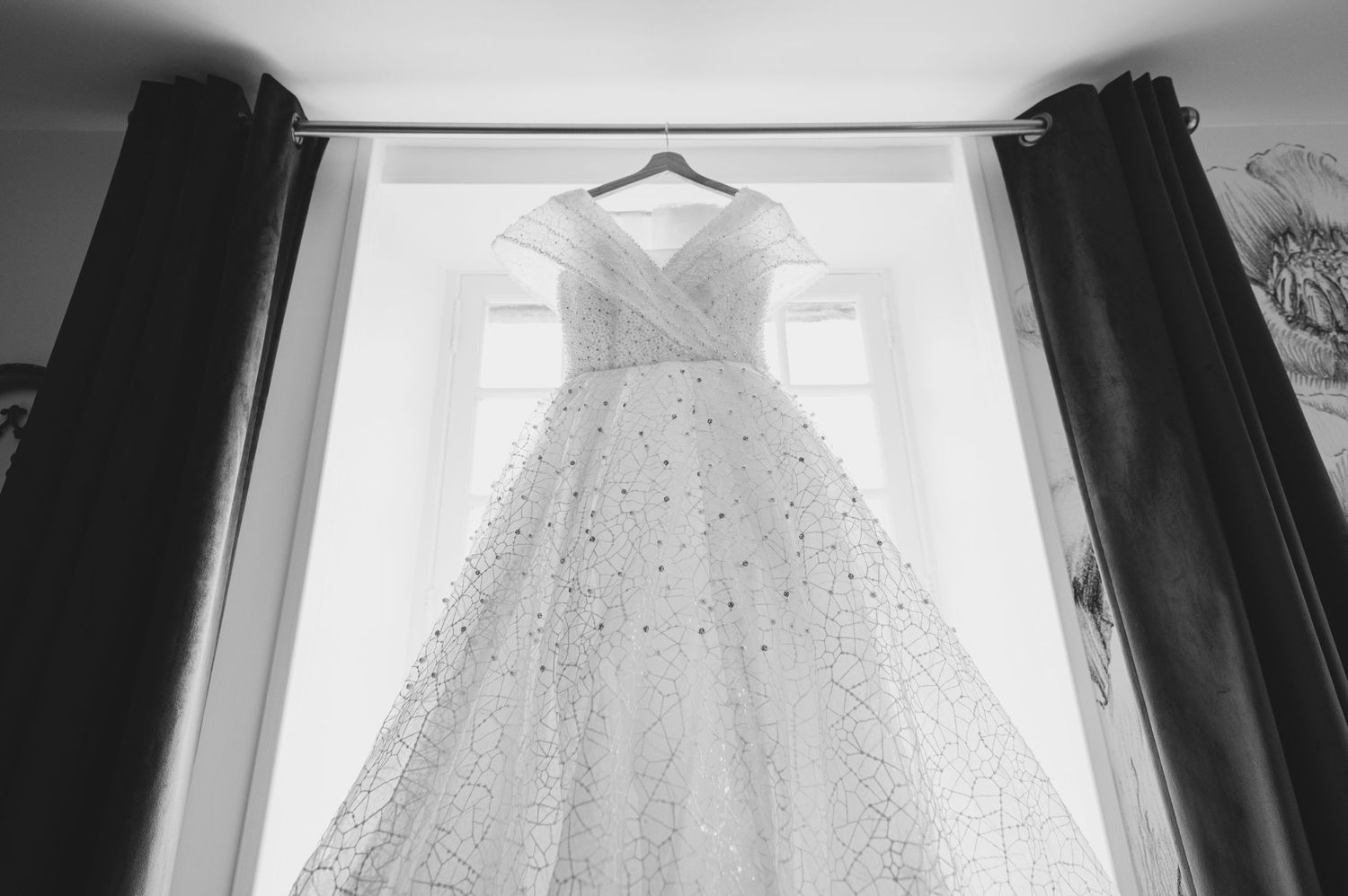 Beautiful ball gown wedding dress hanging in a window, captured in black and white photography.