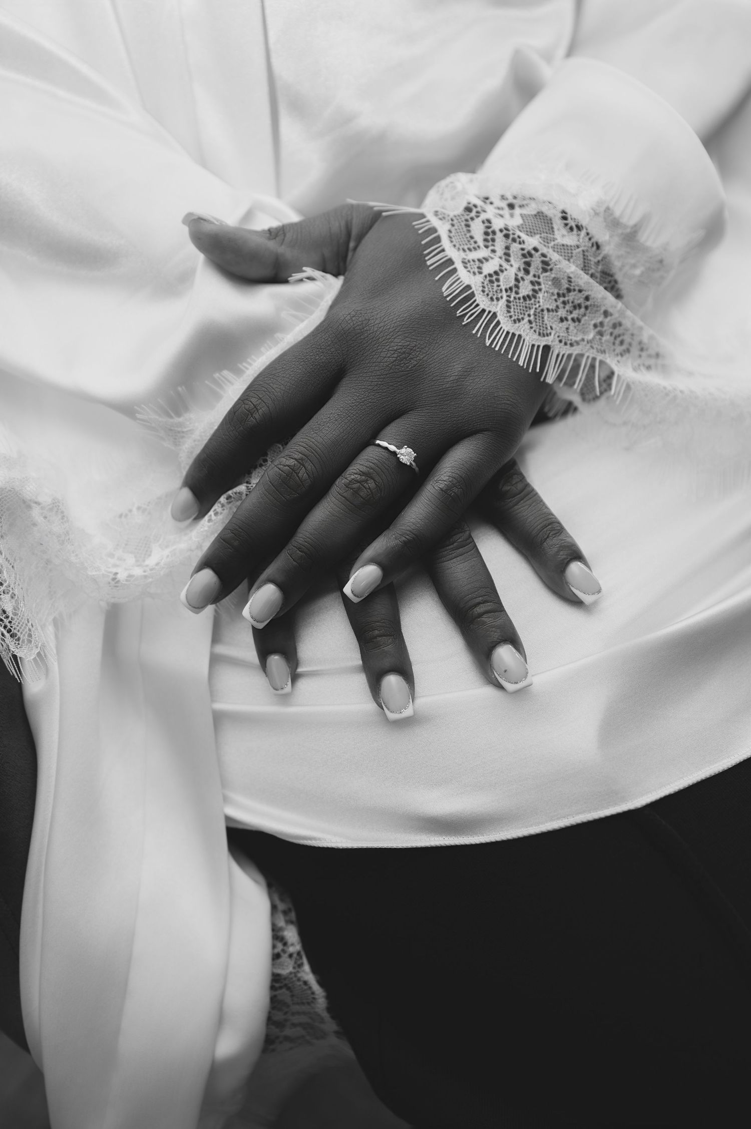 Black and white close-up of bride and groom hands showing diamond engagement ring on wedding day.