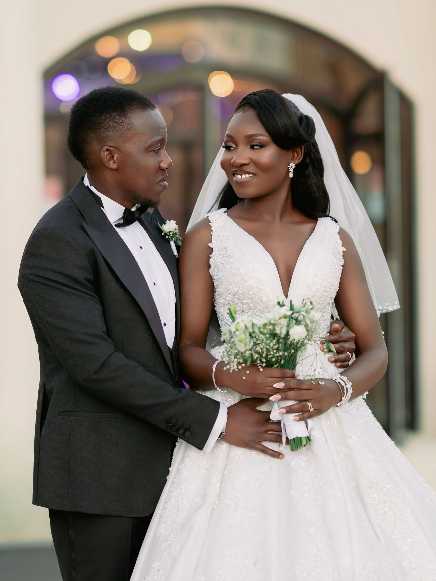 Elegant Black couple on wedding day, bride in V-neck lace ball gown holding a white bouquet.