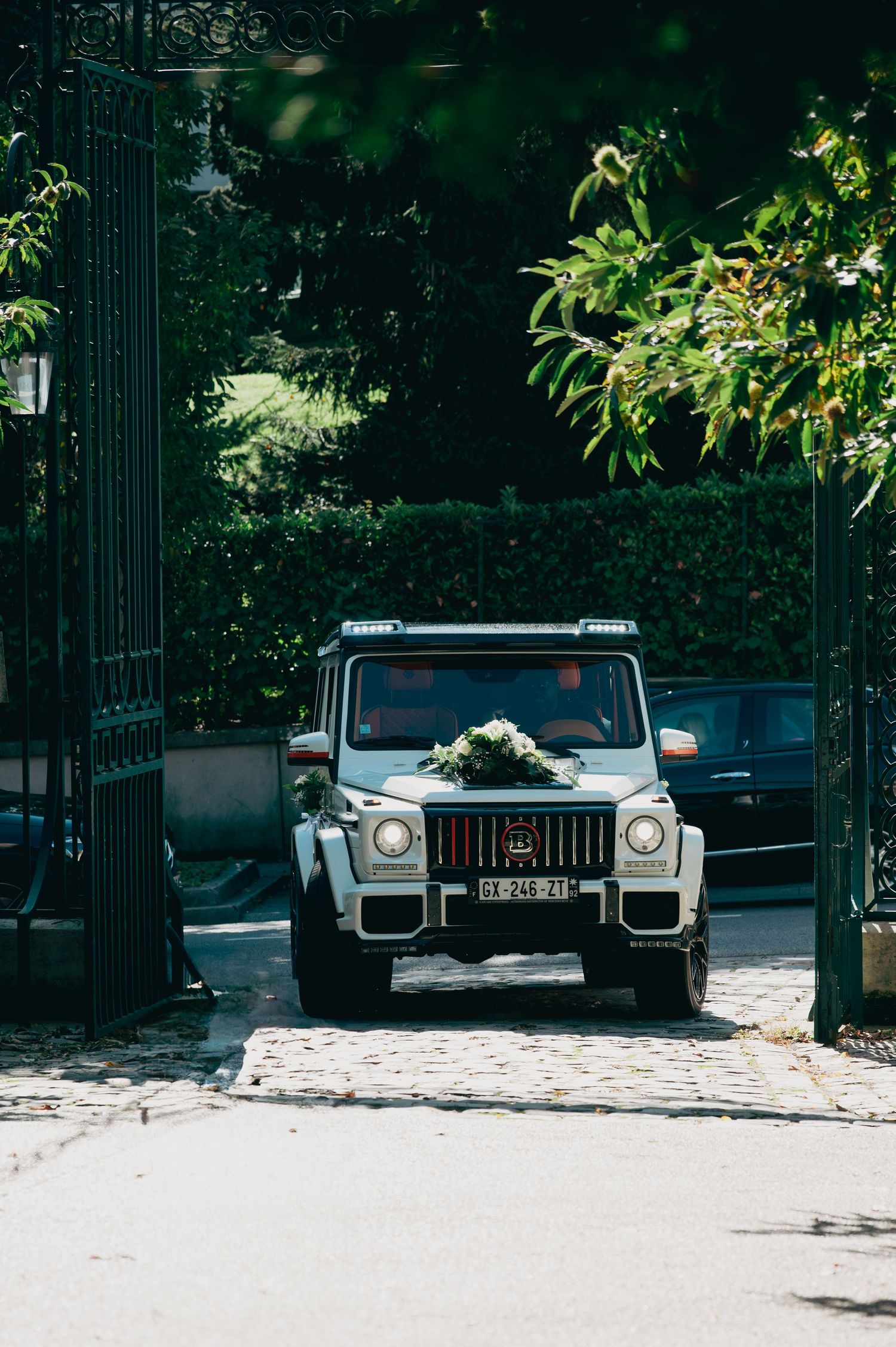 White Mercedes G-Wagon wedding car decorated with floral arrangement entering through iron gates.