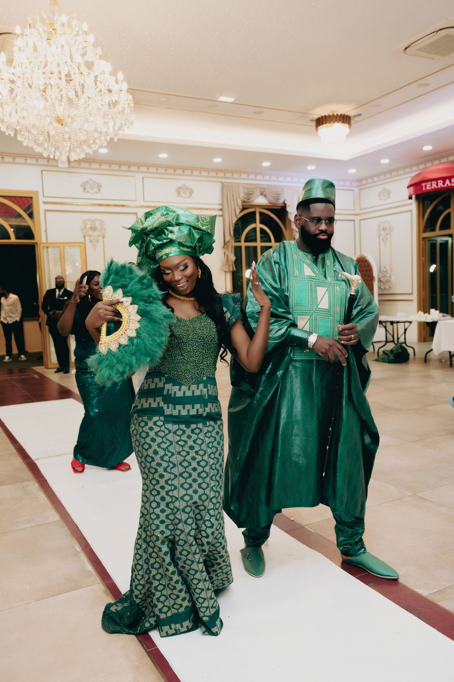 Couple posing in matching green African traditional attire with gele headwrap at wedding reception.