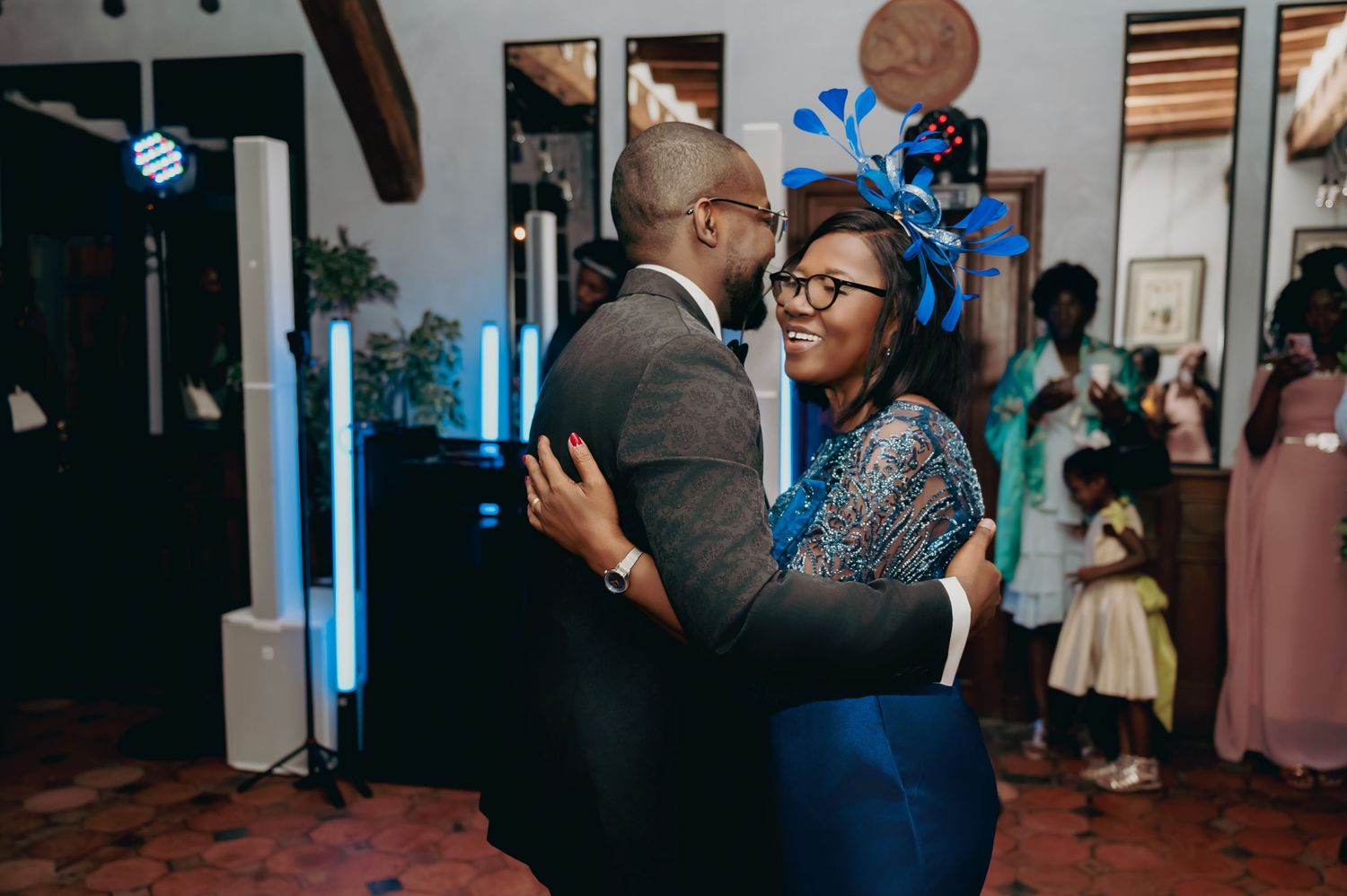 Couple sharing a joyful dance at a wedding reception, woman wearing a blue fascinator hat.