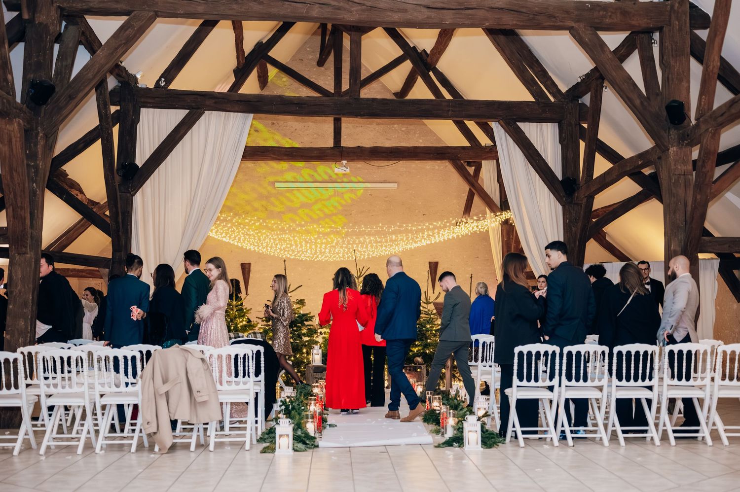 Wedding guests gathered at a Christmas ceremony in a rustic barn venue with exposed timber beams and fairy lights.