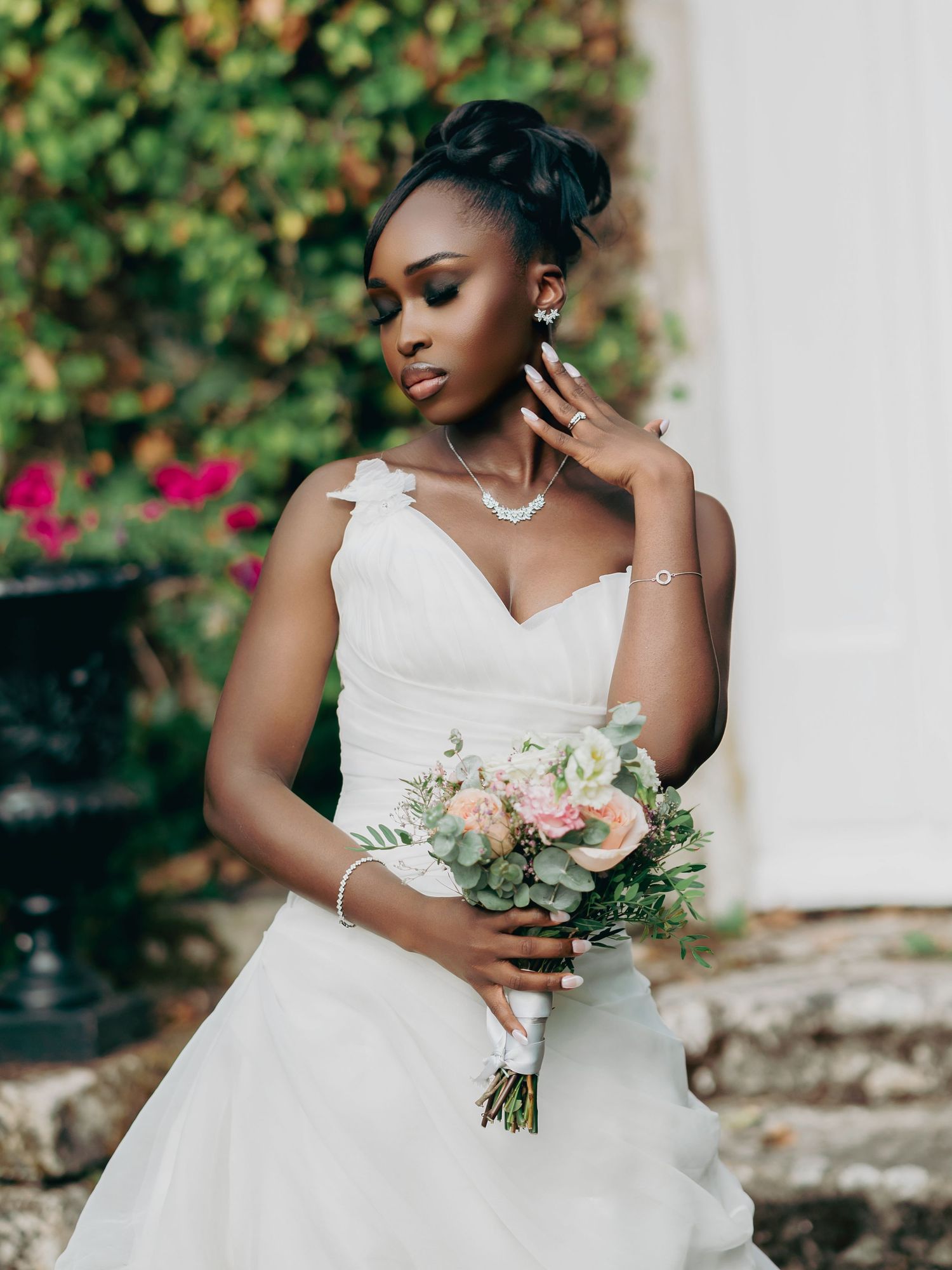 Elegant Black bride in white sweetheart wedding gown holding pink and green bridal bouquet outdoors.