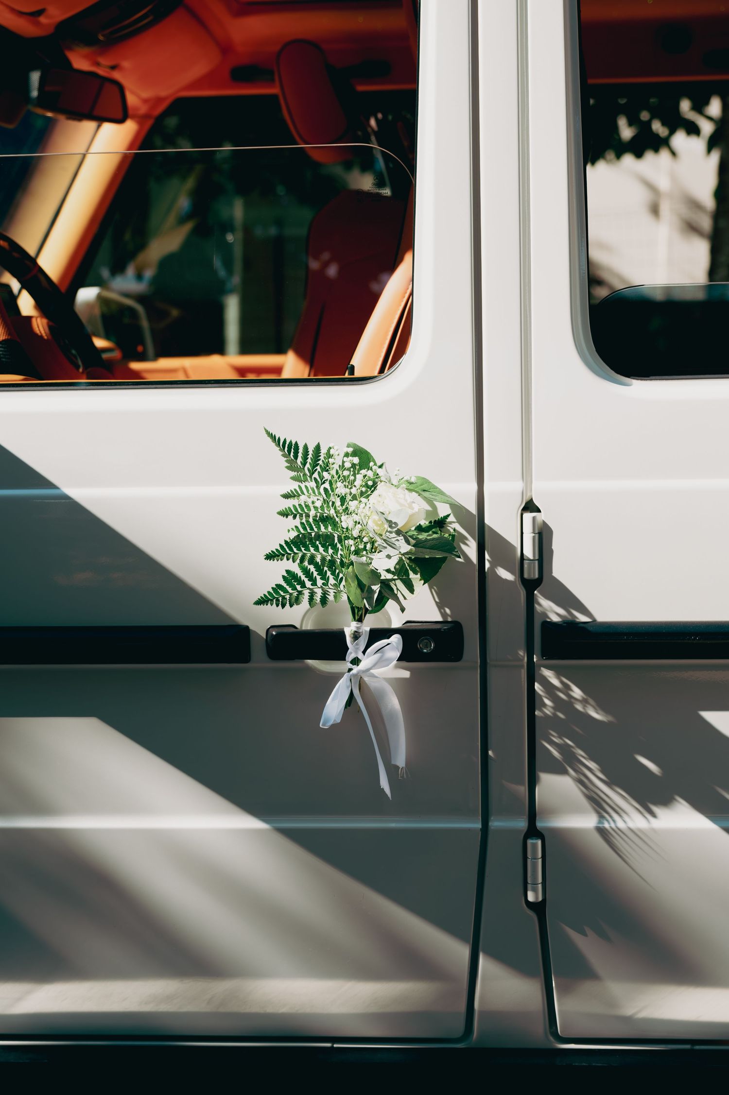 White Mercedes G-Wagon door adorned with elegant greenery and white ribbon wedding decoration.