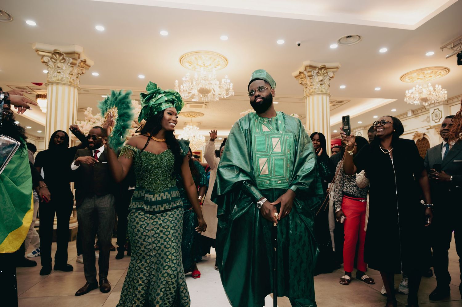 Couple walking in elegant matching green African traditional wedding attire at a grand reception venue.