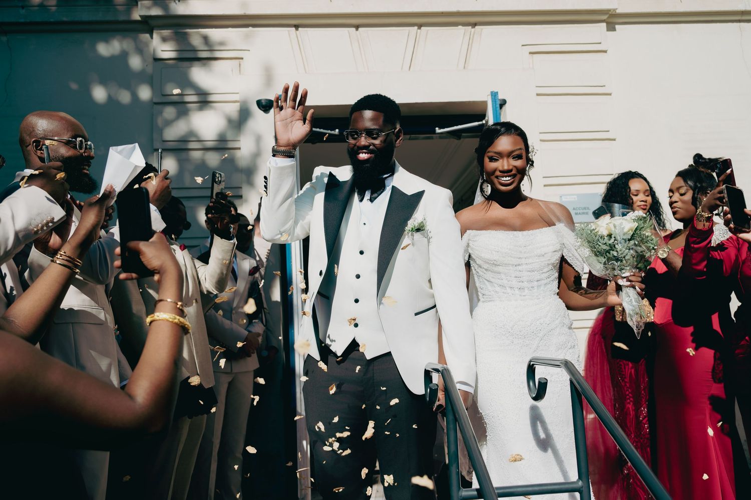 Bride and groom celebrate wedding exit with confetti and cheering guests in elegant attire.