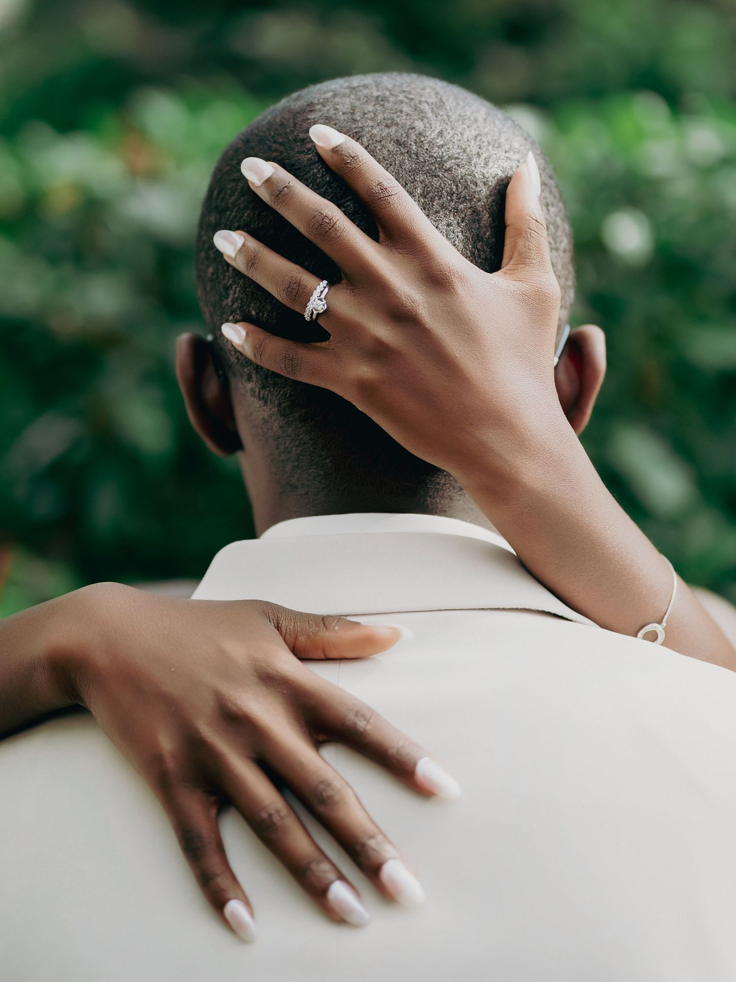 Close-up of bride's hands with white manicure and diamond ring resting on groom's head at wedding.