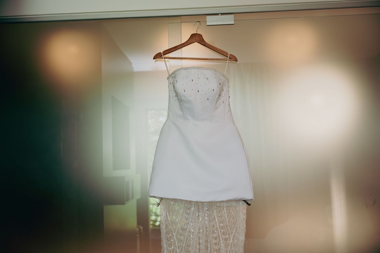 Elegant strapless white wedding dress with lace skirt hanging on a wooden hanger.