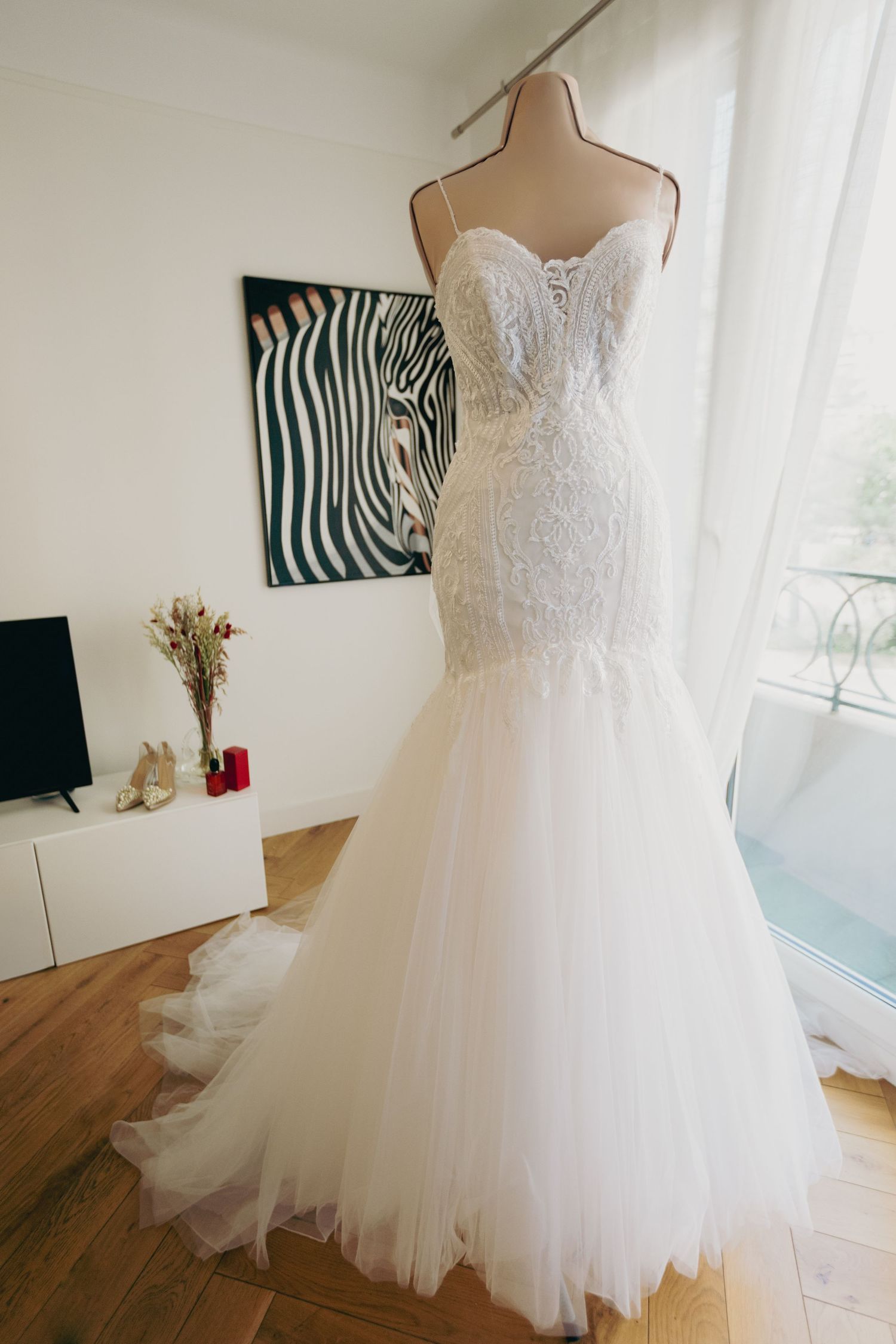 Mermaid lace wedding dress with tulle skirt displayed on mannequin near bright window.