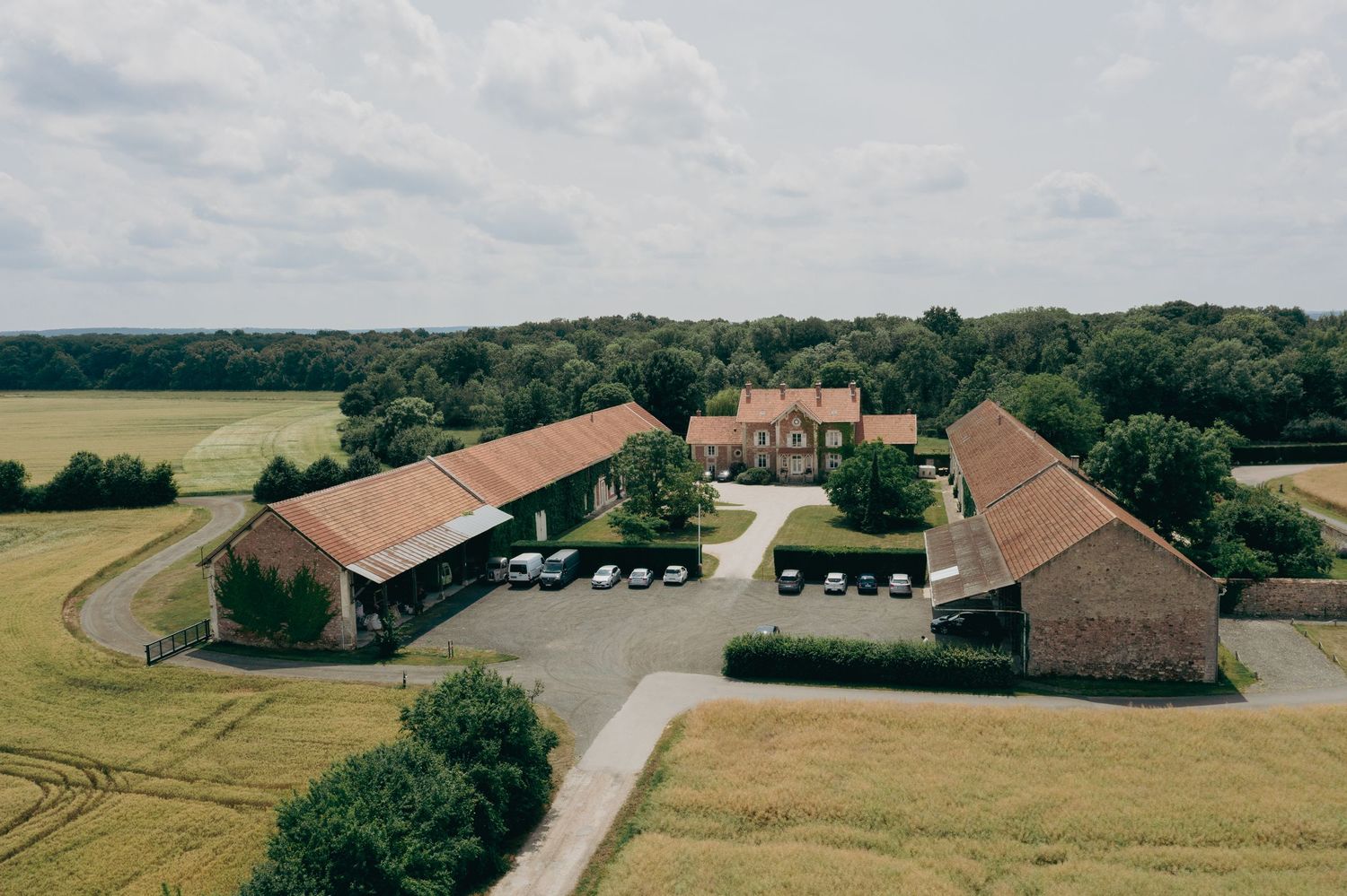 Aerial view of rustic countryside wedding venue with brick barn buildings surrounded by green fields.