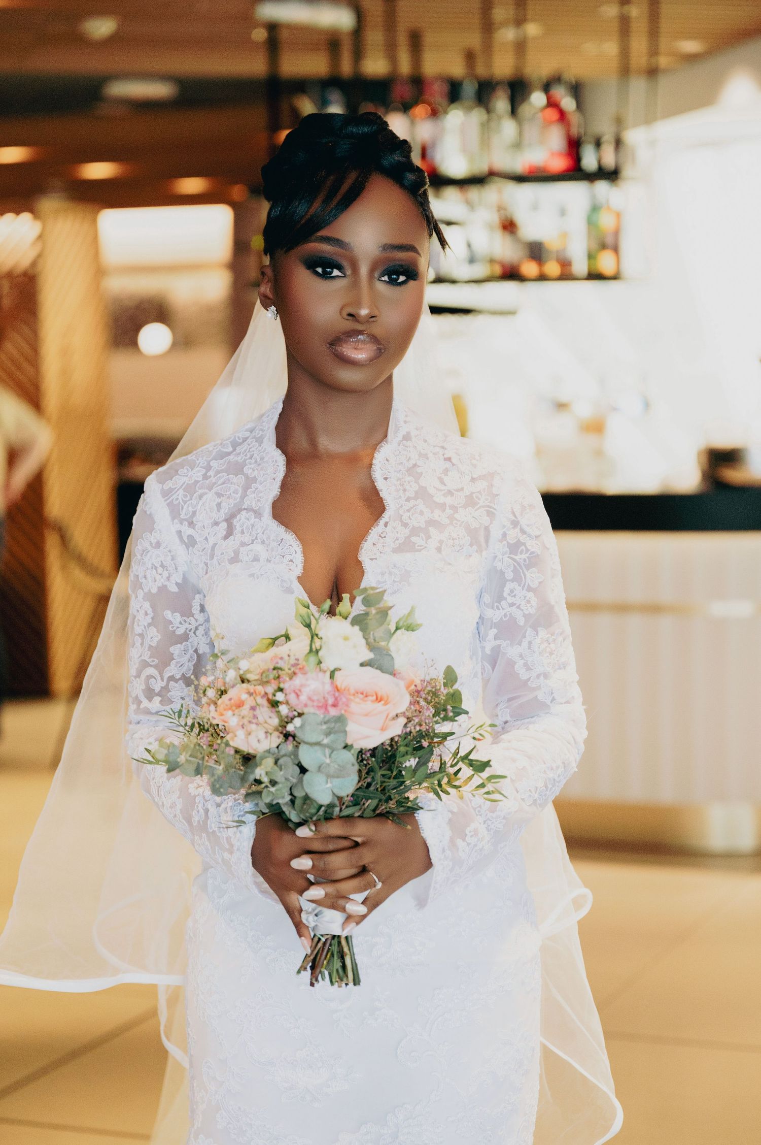 Stunning Black bride in long-sleeve lace wedding gown holds pink and white bouquet with veil.