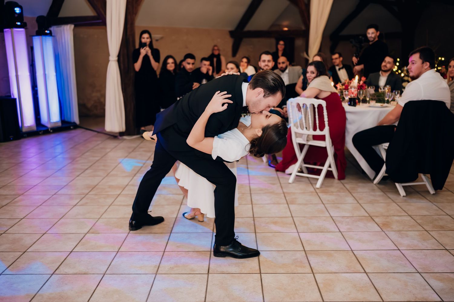 Groom dips bride dramatically on the dance floor surrounded by wedding guests.