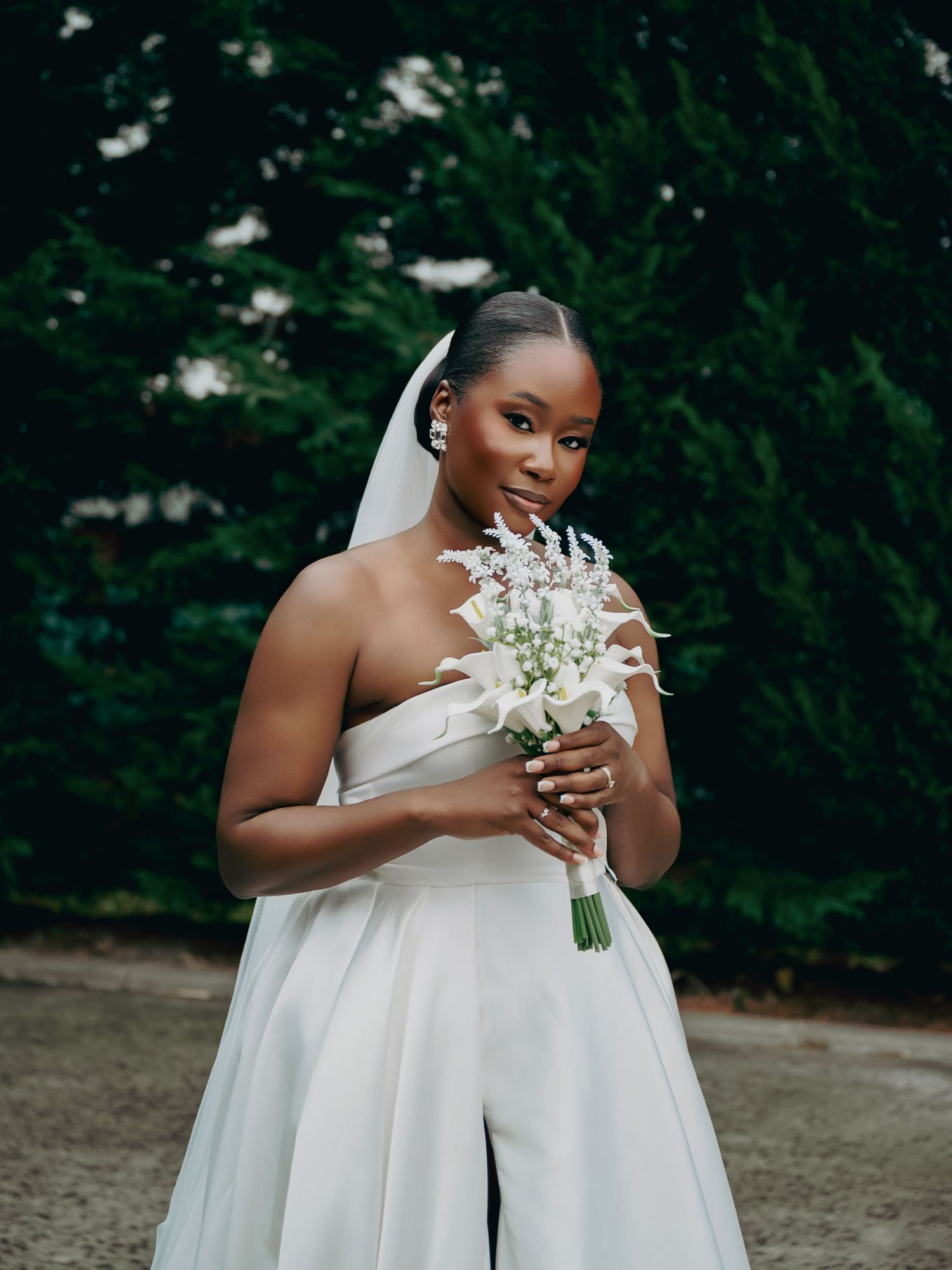 Beautiful Black bride in strapless white gown smelling white floral bouquet with drop earrings and veil.