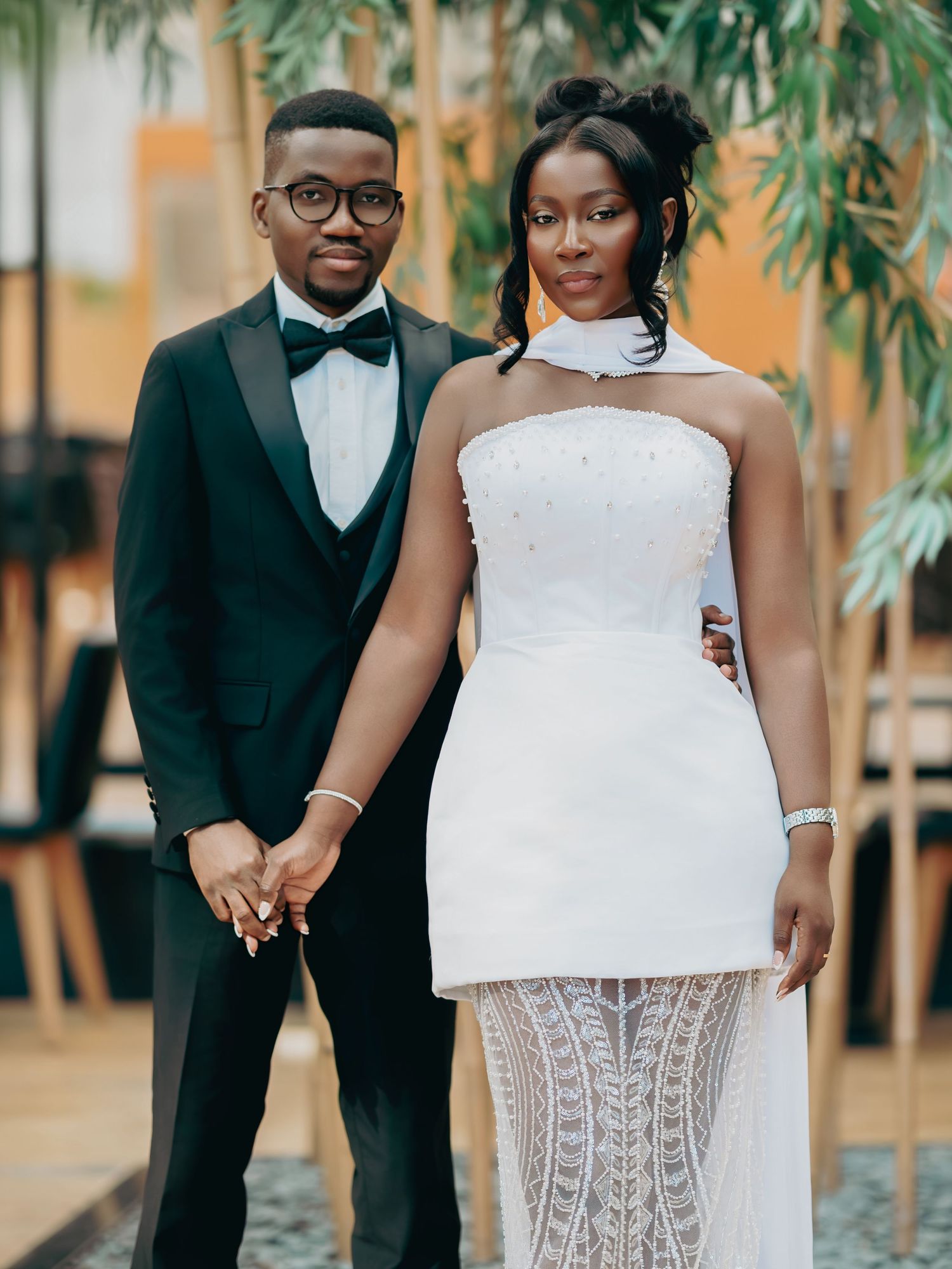 Wedding couple holding hands, groom in black tuxedo and bride in white lace gown.