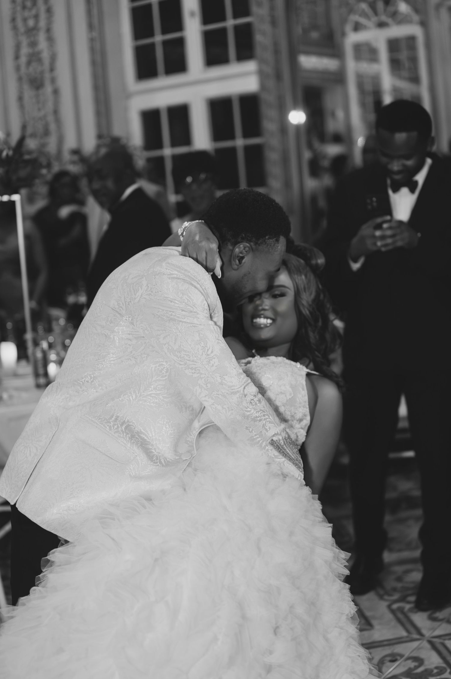 Black and white photo of Black bride and groom sharing tender embrace on dance floor at reception.