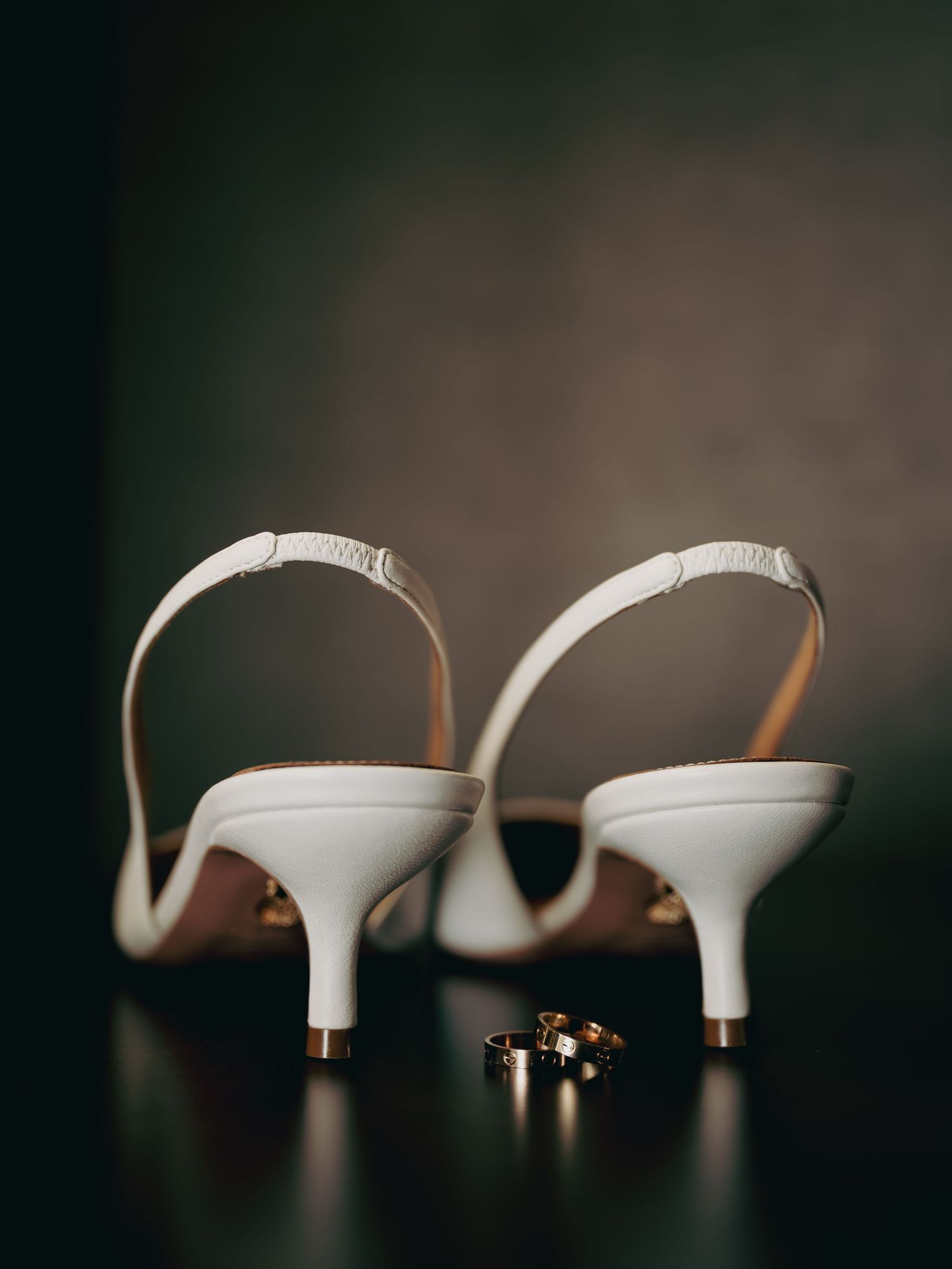 White kitten heel slingback wedding shoes with two gold wedding bands placed between them.