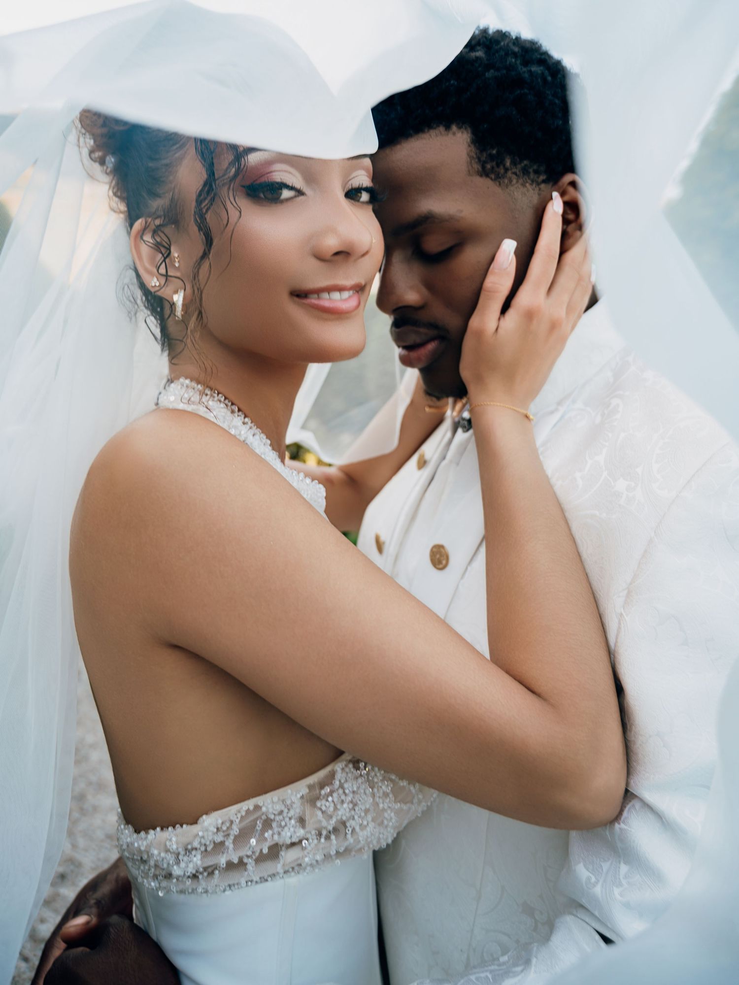 Bride and groom share an intimate moment under a flowing veil on their wedding day.