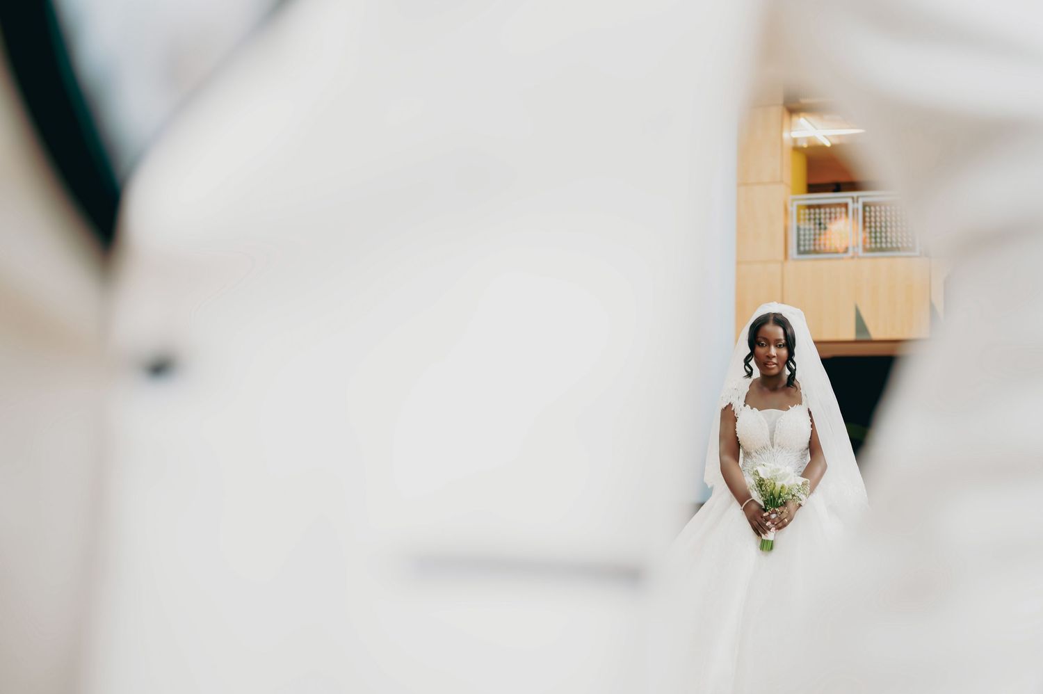 Bride in white gown and veil holding bouquet framed between two figures in white suits.