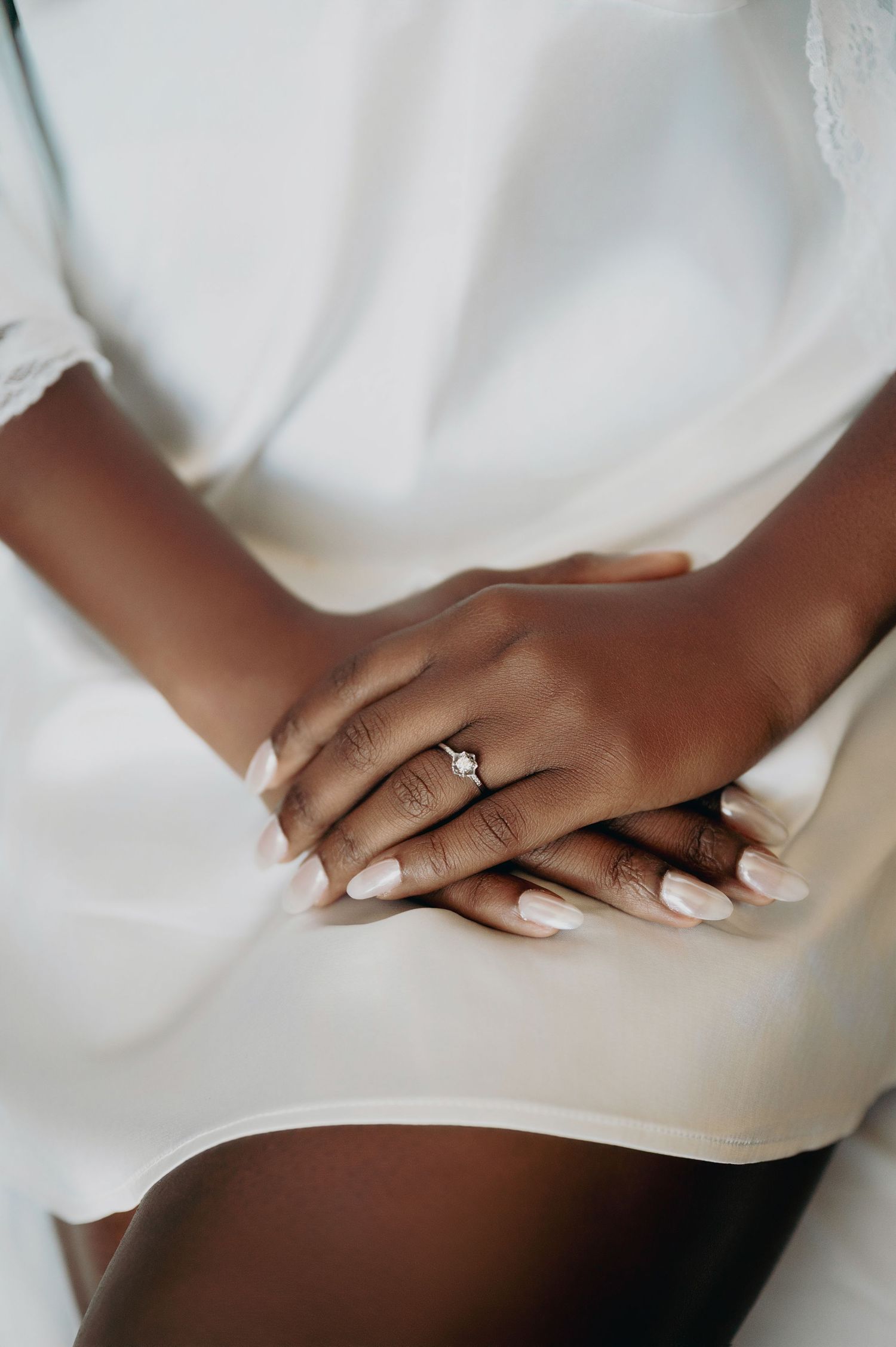 Bride's hands folded in lap showing diamond engagement ring and white manicure.