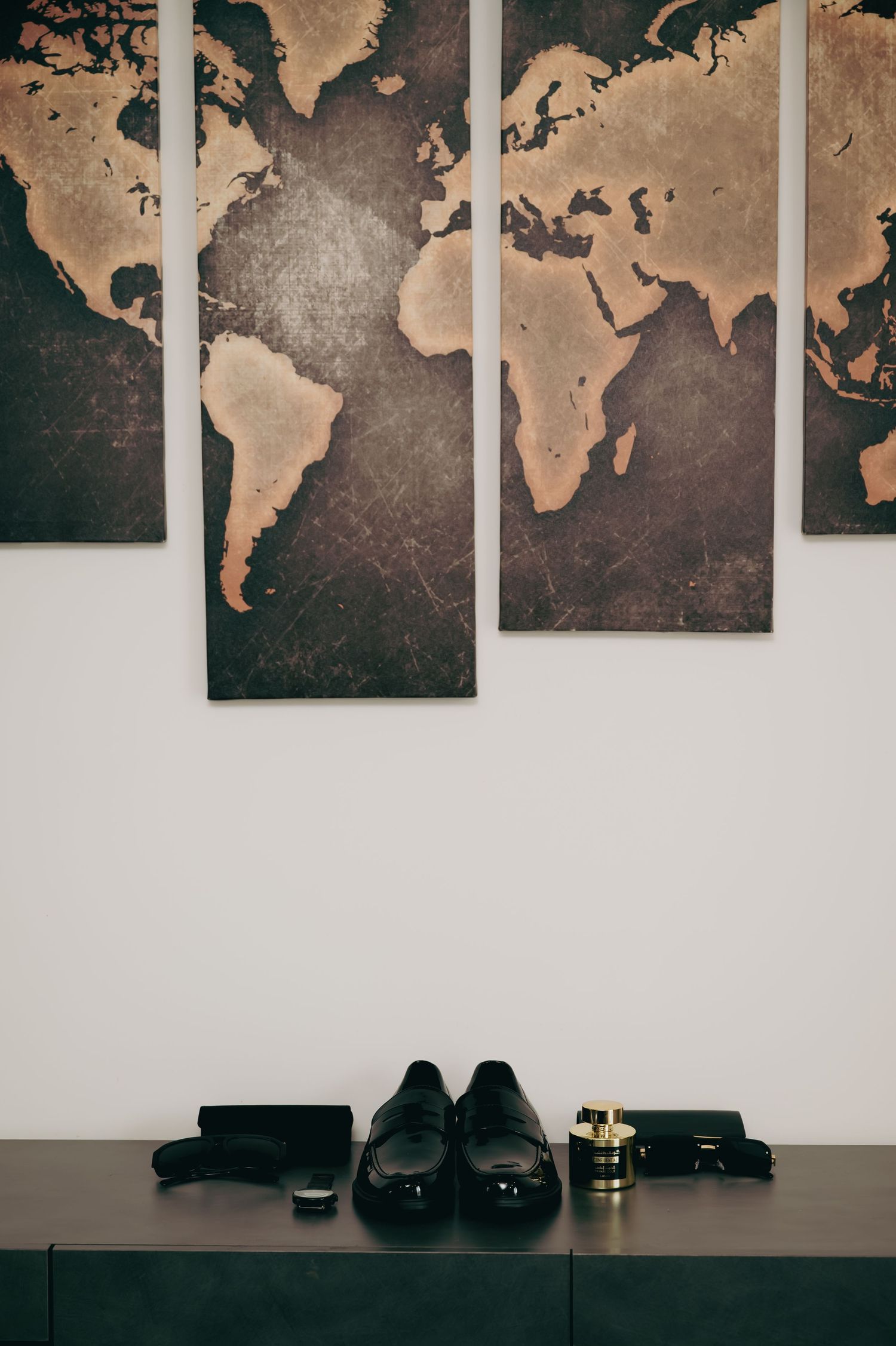 Black dress shoes, cologne, and accessories arranged under a world map wall art display.