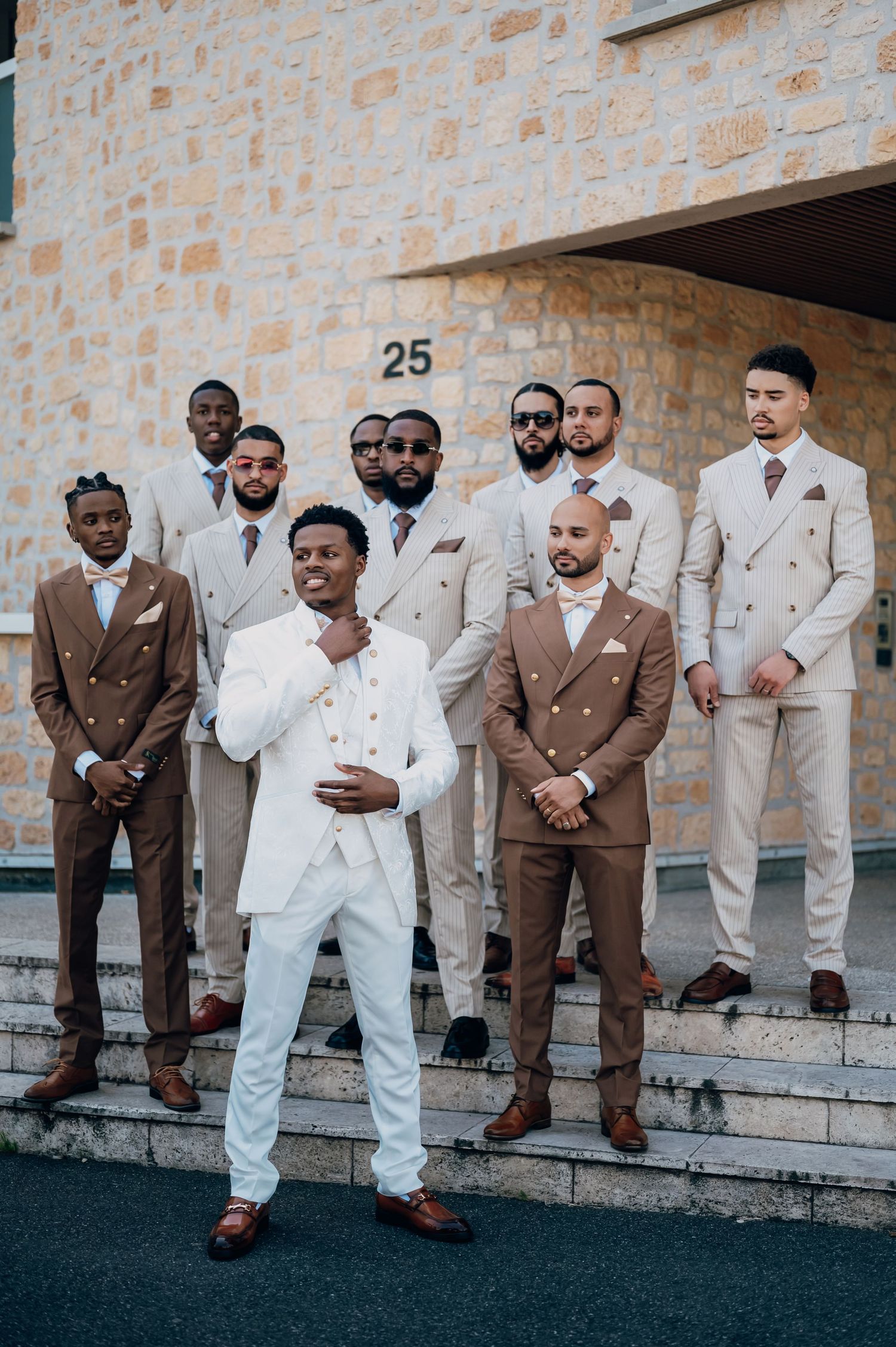Groom in white suit poses with groomsmen wearing coordinated tan and brown double-breasted suits outside building 25.