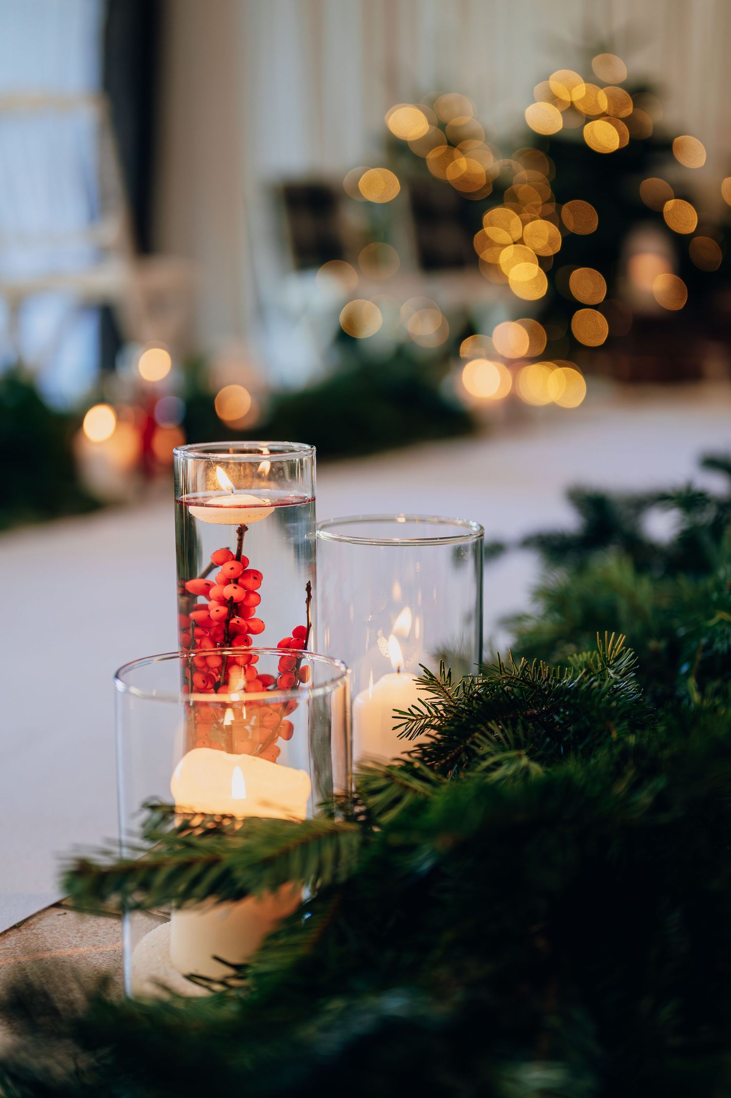 Elegant Christmas wedding table centerpiece with candles in glass holders, red berries, and pine branches.