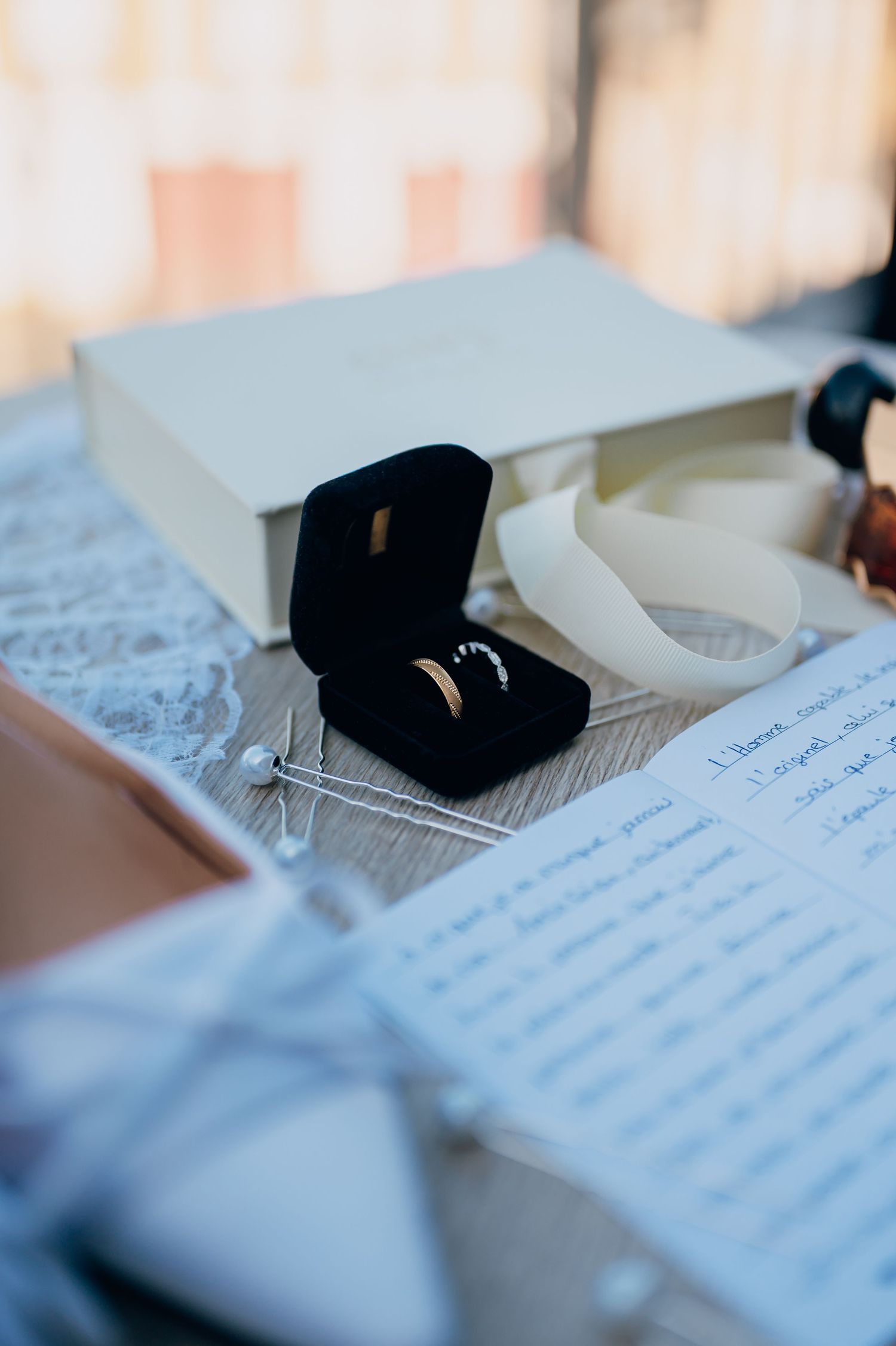 Wedding rings in black velvet box beside handwritten vows and white gift box on wooden table.