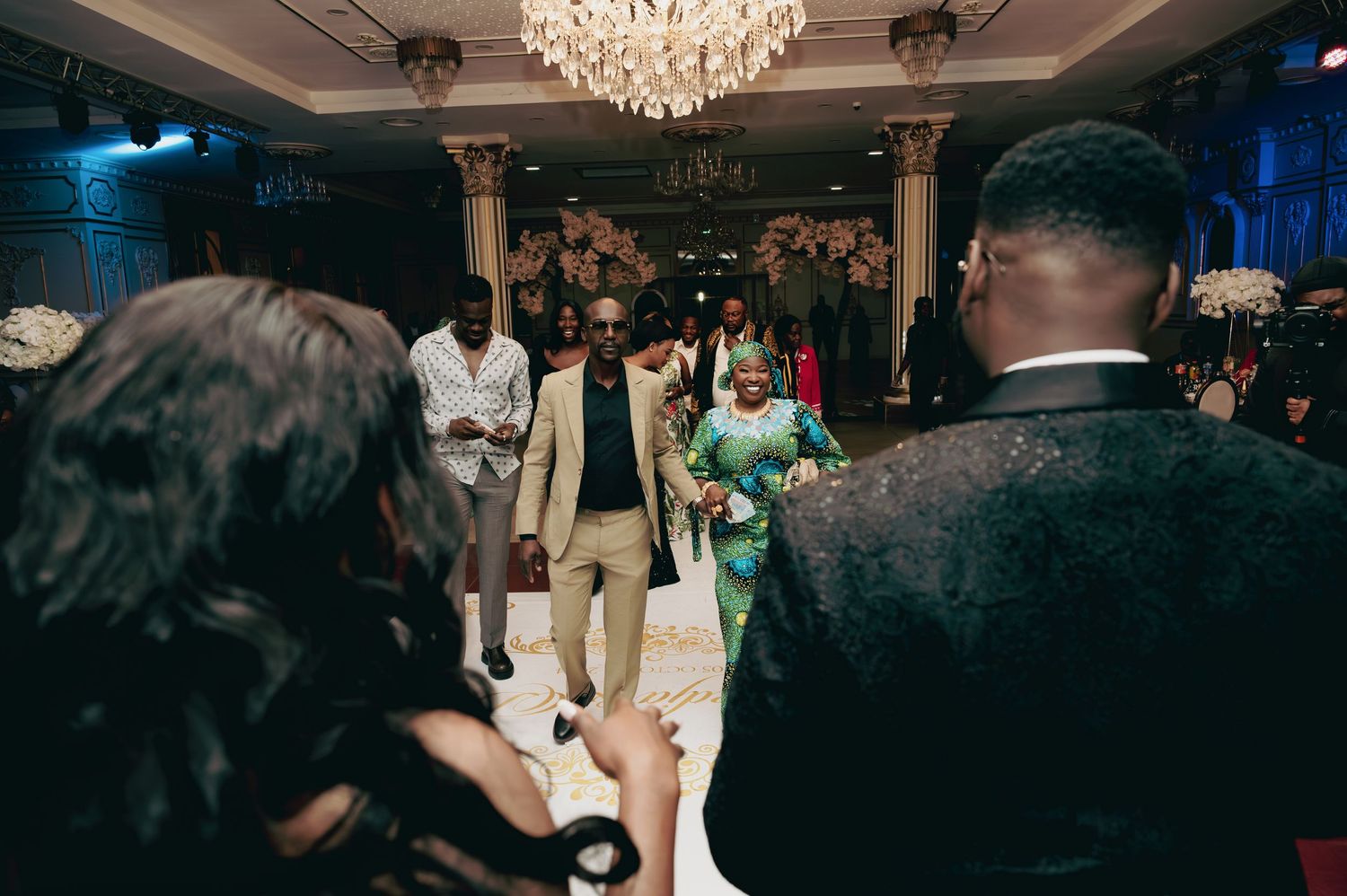 Wedding guests walk onto dance floor during elegant ballroom reception celebration.