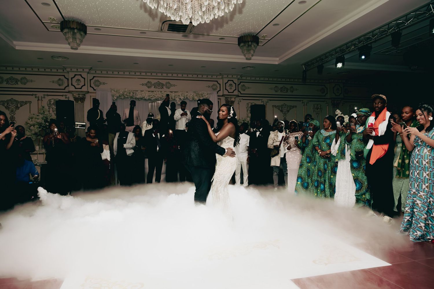 Newlyweds share first dance surrounded by fog on elegant ballroom dance floor.