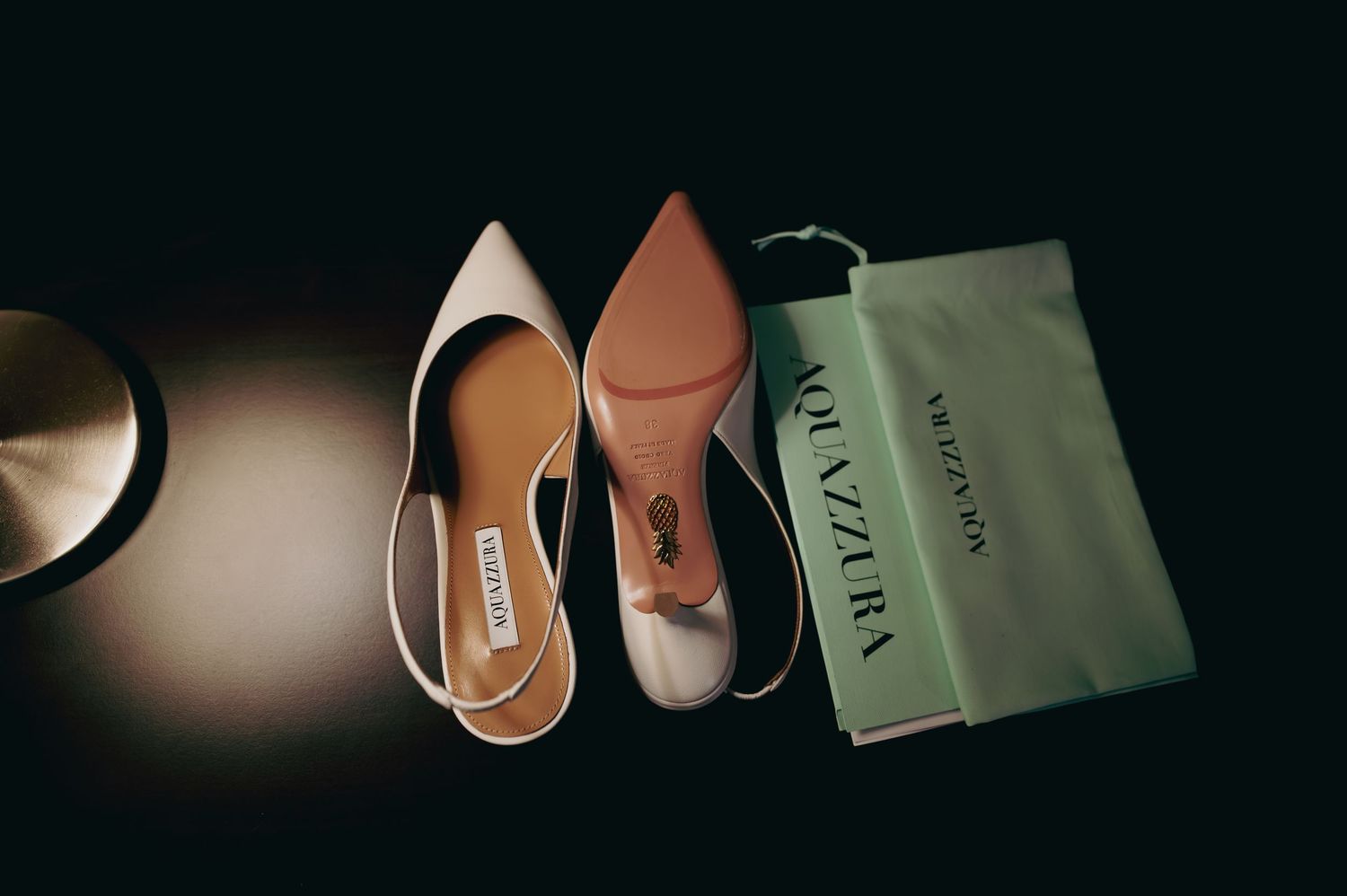 Aquazzura designer bridal heels displayed with dust bag on dark surface.