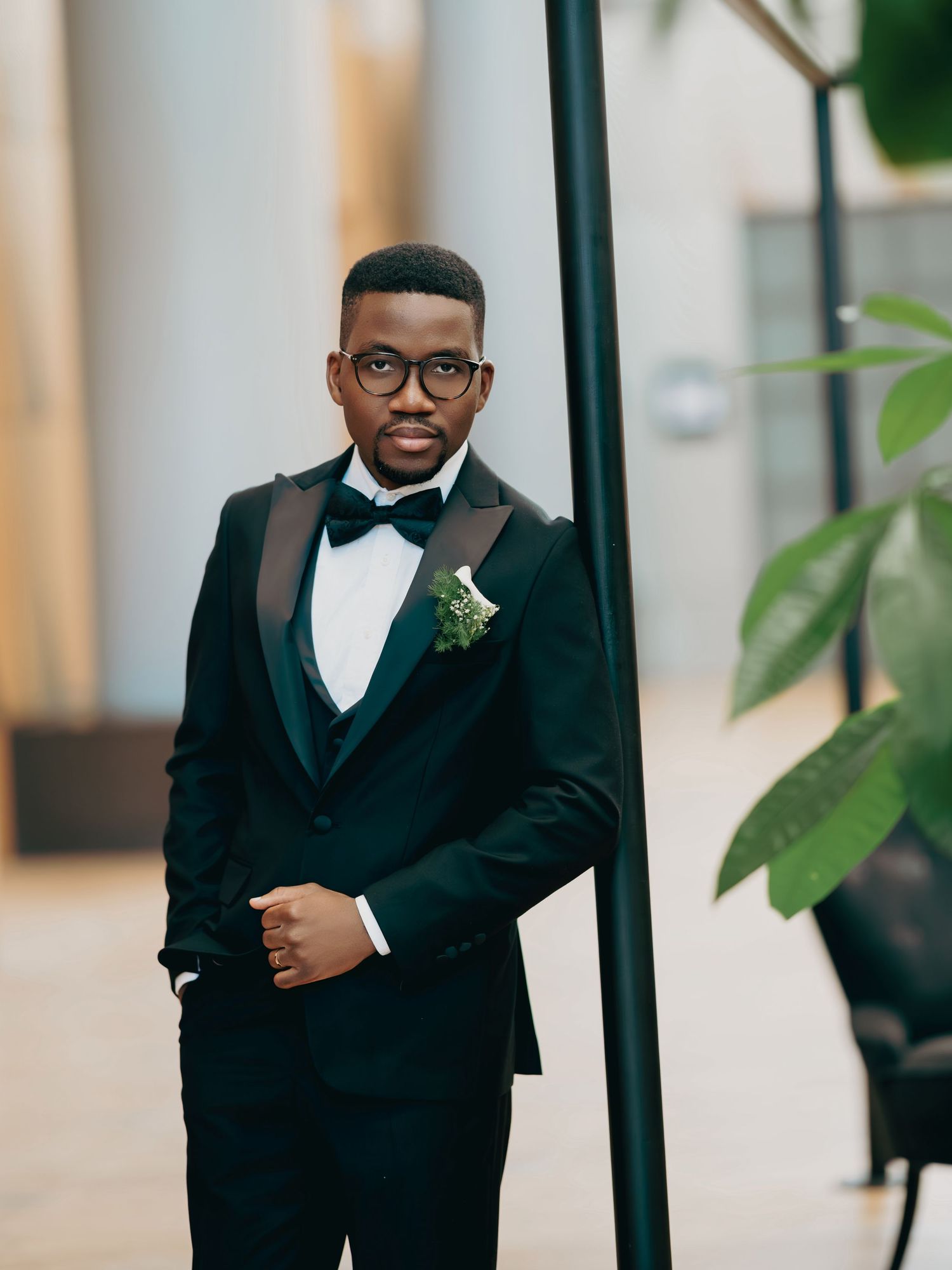 Dapper groom in black tuxedo with bow tie and boutonniere posing indoors at wedding.