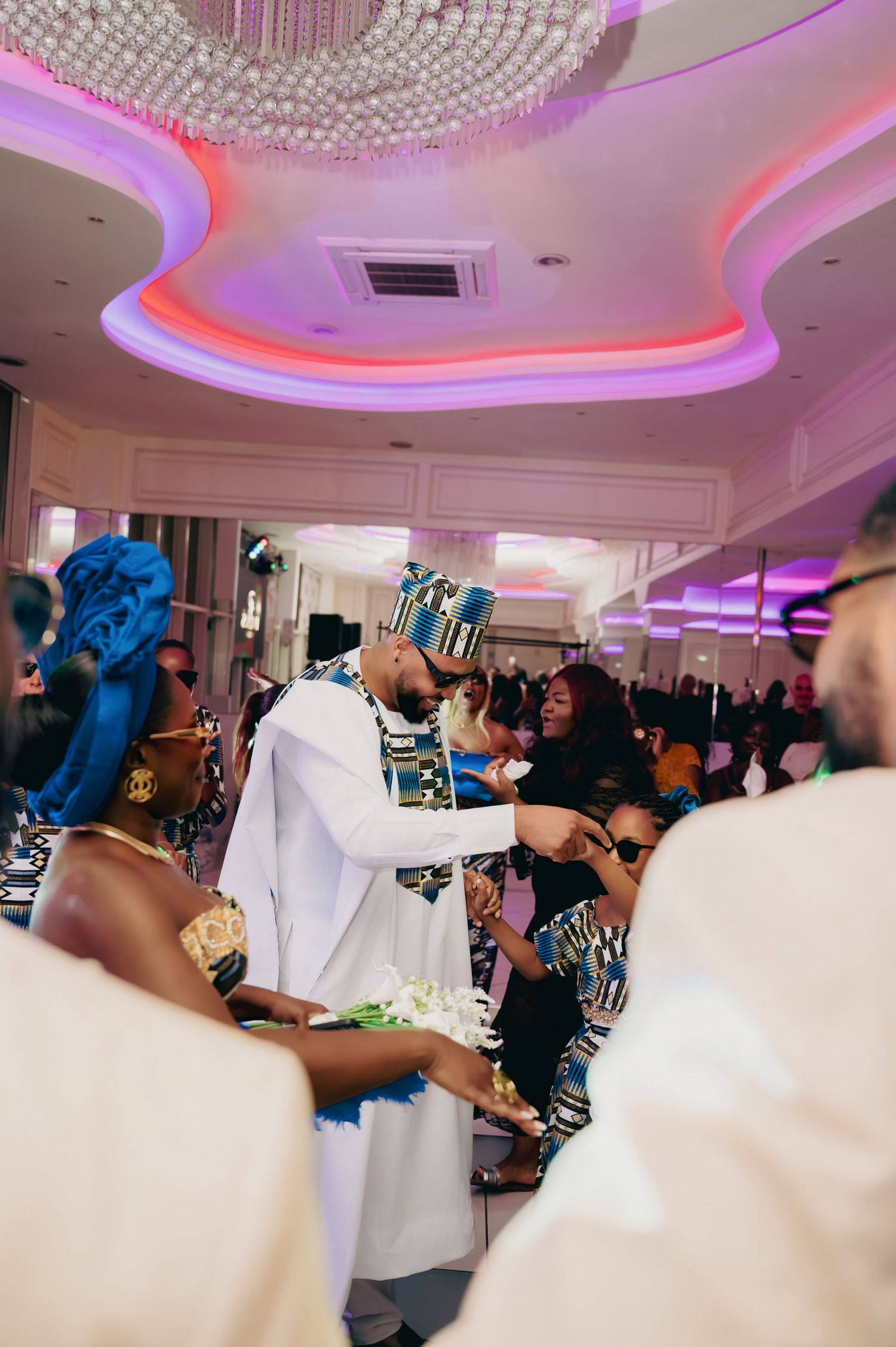 Bride and groom in traditional African wedding attire share a tender moment at reception.
