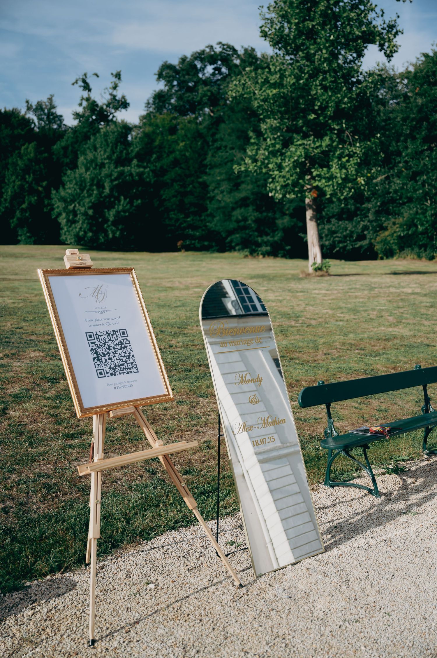 Outdoor wedding welcome sign on easel with QR code and mirrored sign on gravel path.