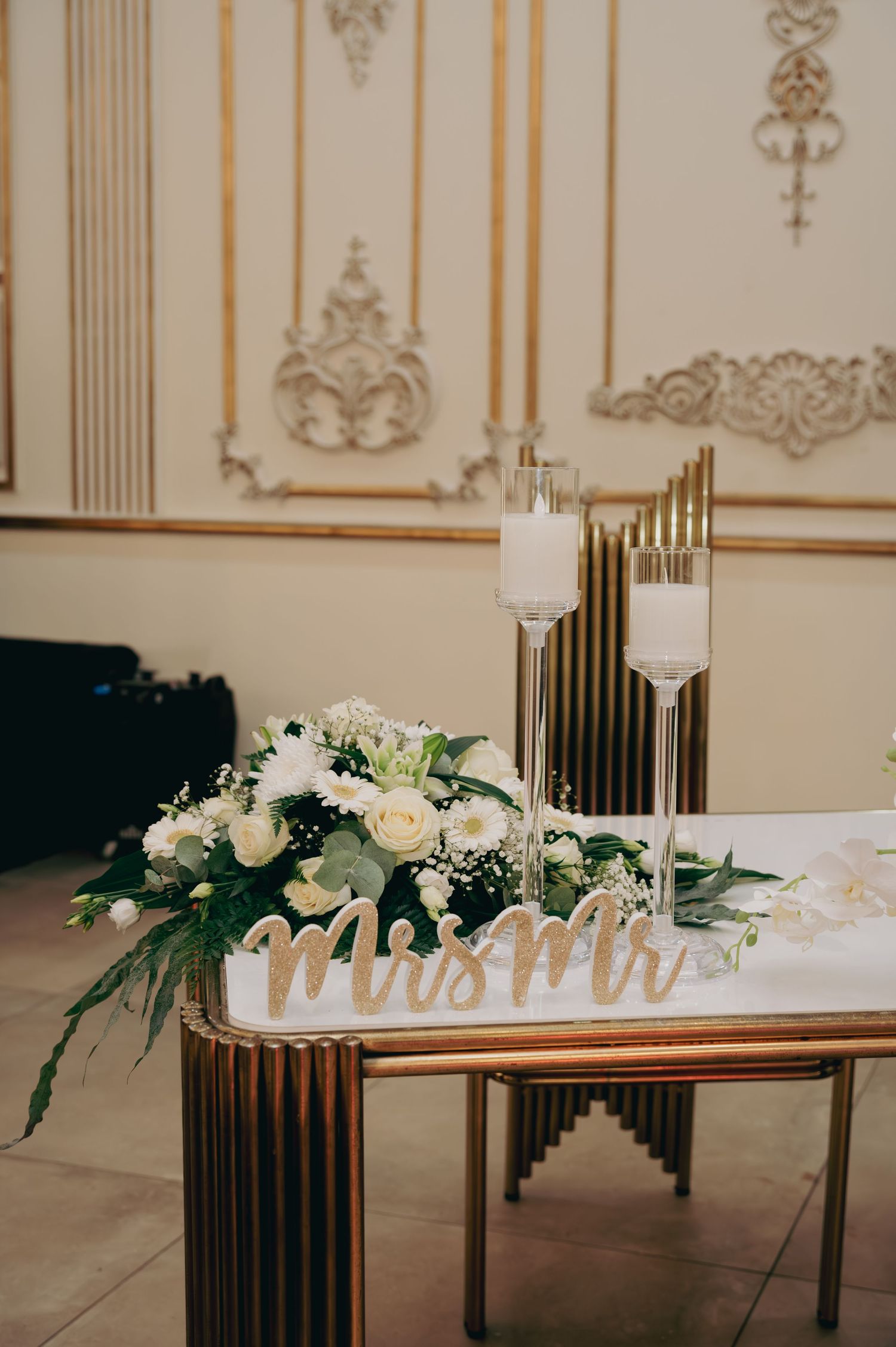 Wedding sweetheart table with Mrs and Mr sign, white roses, and gold candle holders.