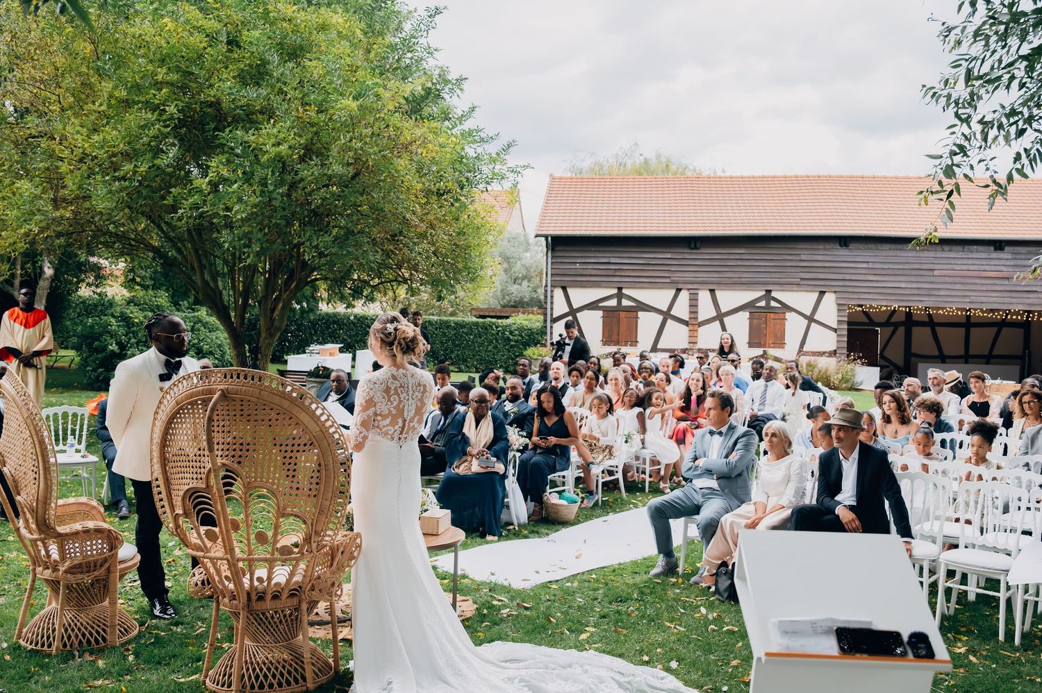 Bride standing at the altar of a boho outdoor wedding ceremony with guests seated on white chairs.