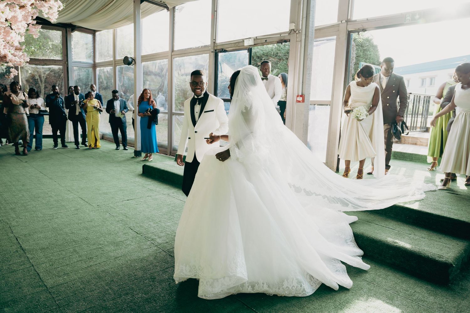 Bride and groom share first dance in a bright glass-windowed venue surrounded by wedding guests.