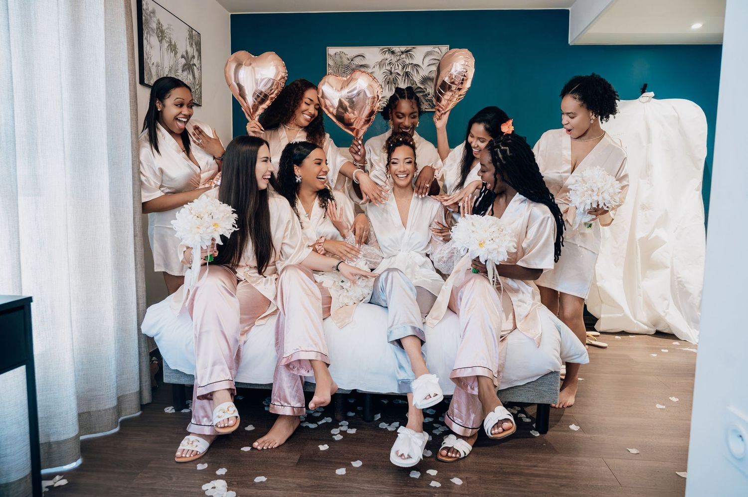 Bride laughing with bridesmaids in pink robes celebrating with confetti and balloons.