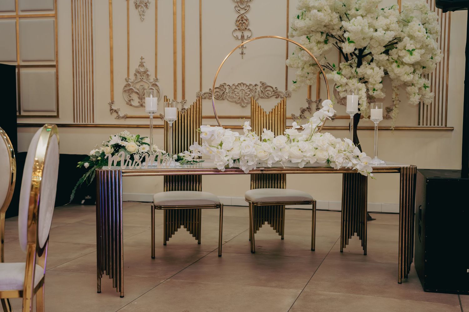 Wedding sweetheart table adorned with white orchids, gold accents, and floral arrangements.