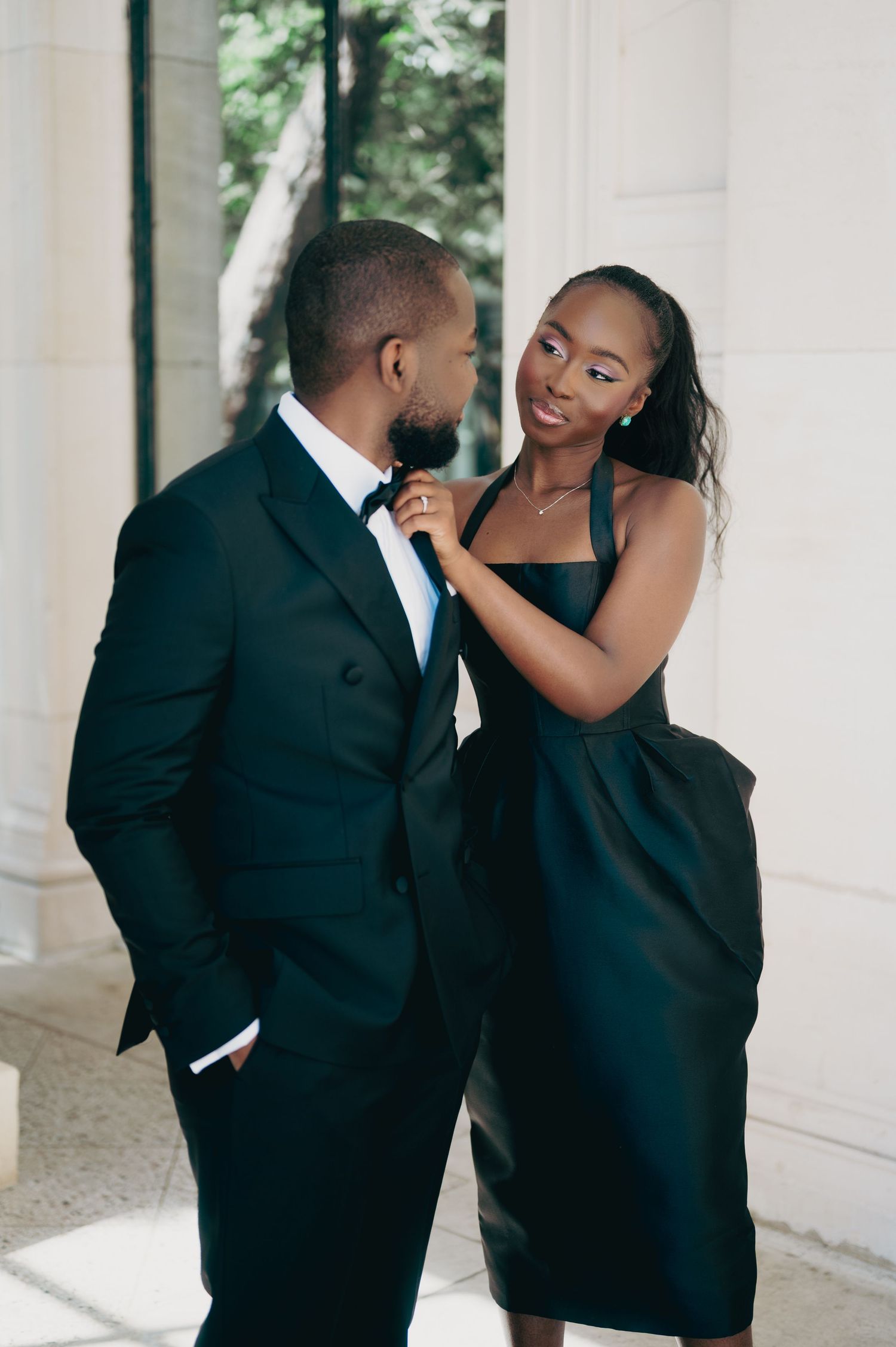 Woman adjusting mans bow tie while sharing an intimate glance during an elegant dark green themed engagement session.